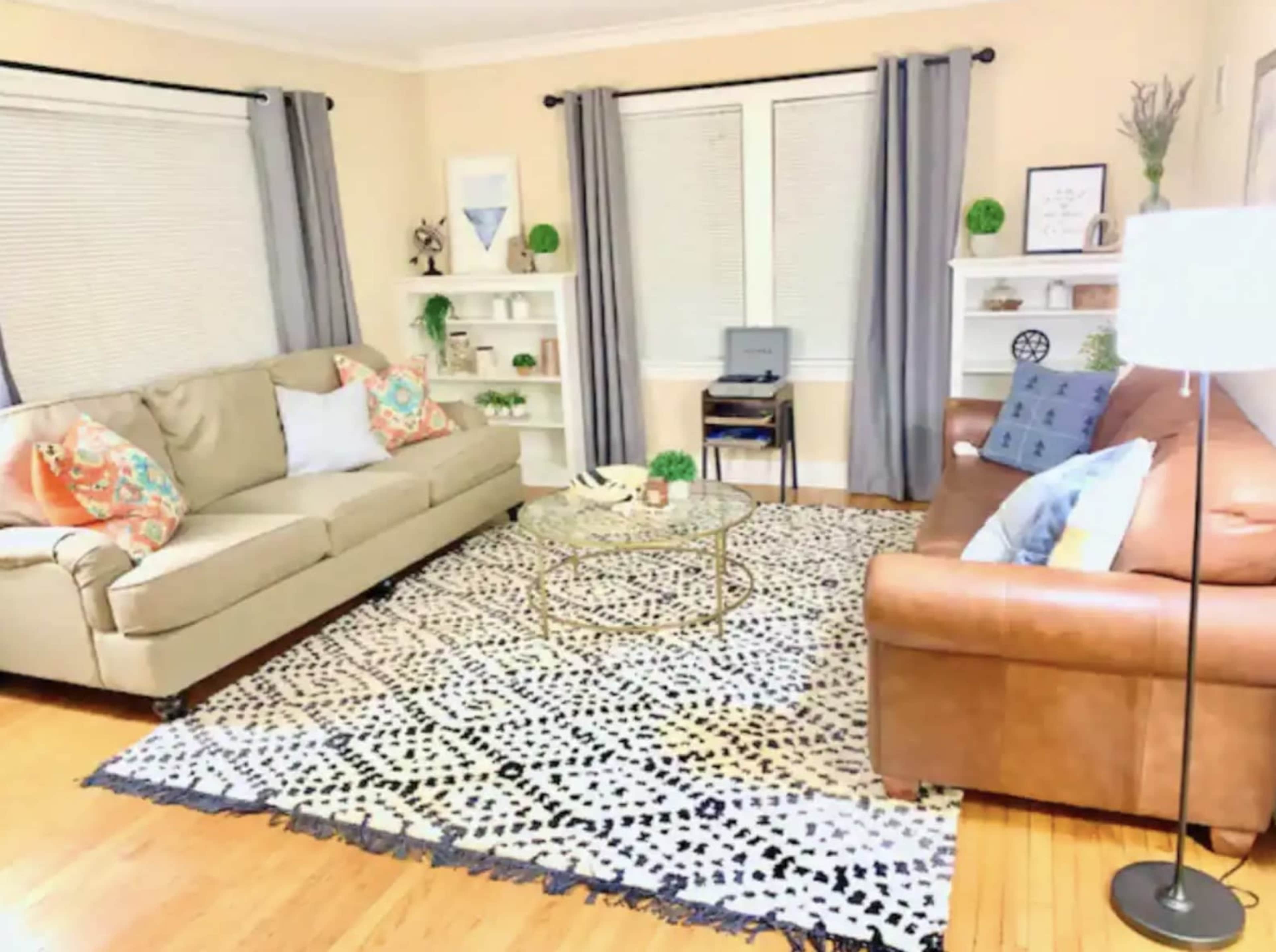 The living room features two sofas, a round coffee table, and shelves against the walls, all set on a patterned area rug.
