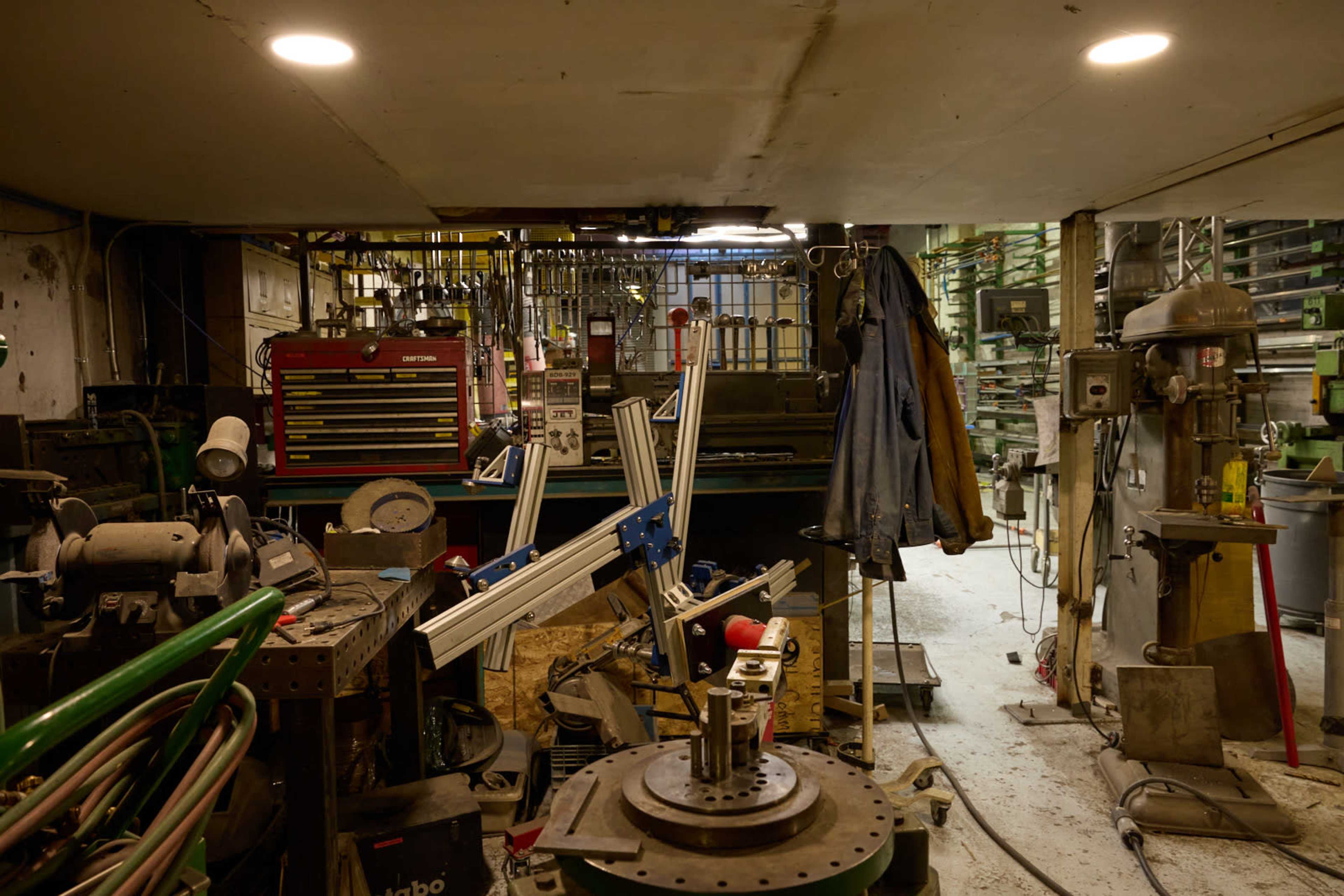 The image shows a cluttered workshop filled with various tools, machinery, and supplies, including a tool chest and workbench.