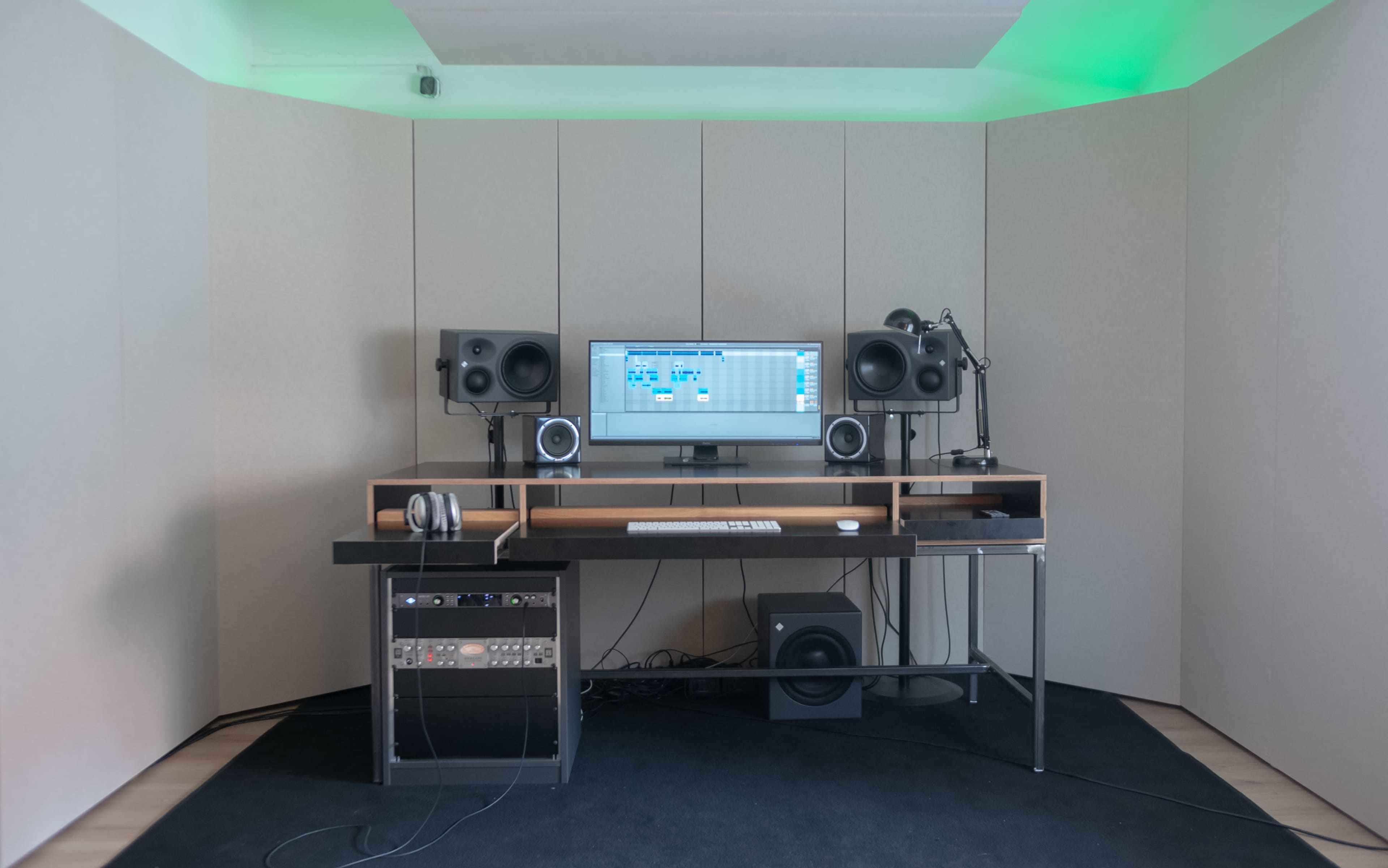 A modern music production studio features a desk with a computer monitor, audio speakers, and sound equipment against soundproofed walls.