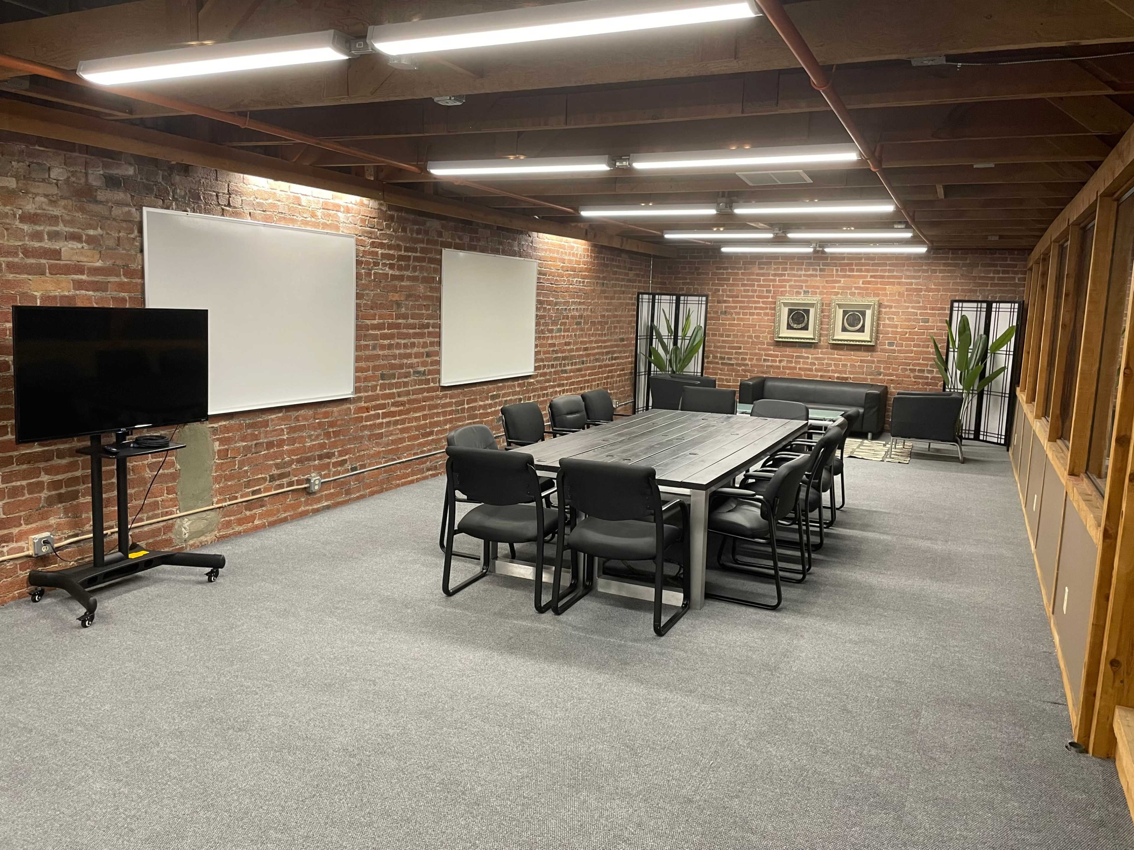 A modern conference room featuring a long table surrounded by black chairs, with brick walls and large windows.