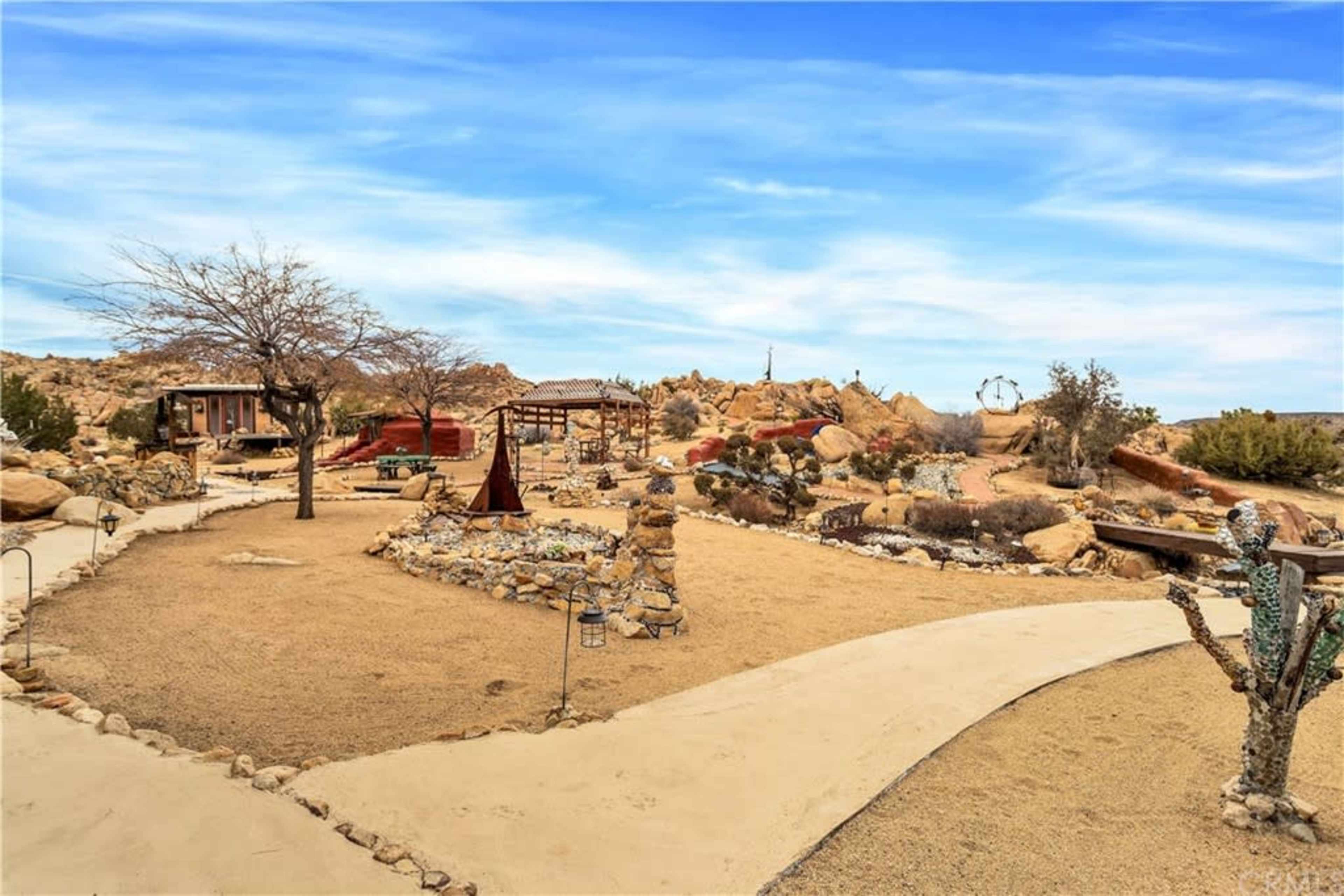 The image shows a landscaped desert area featuring rock formations, walking paths, and a gazebo, surrounded by sparse vegetation.