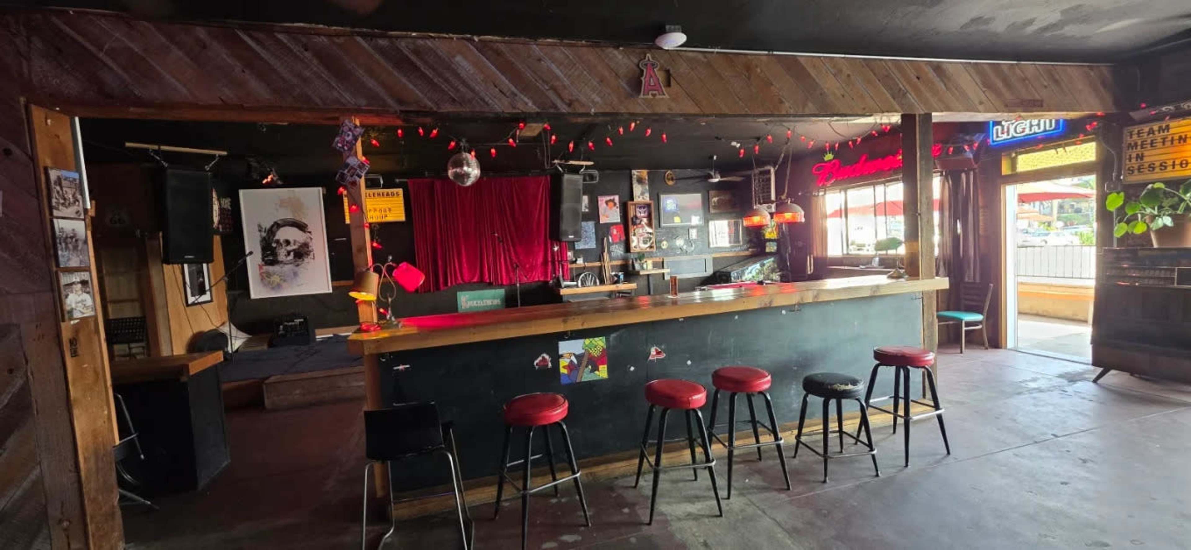 The image shows the interior of a bar with a counter, several black and red stools, and decorations including a disco ball and red lights.