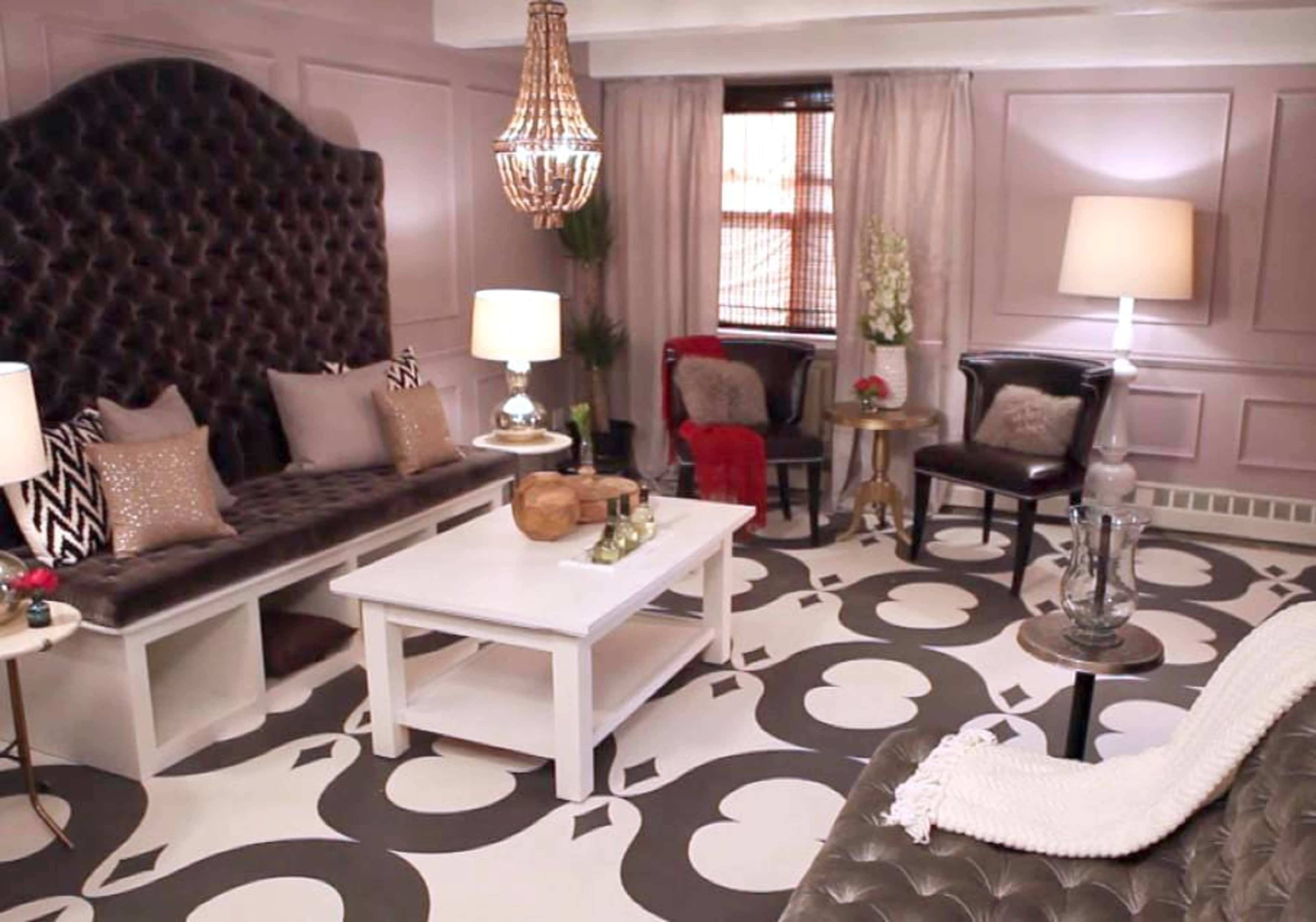 The room features a velvet tufted sofa, a white coffee table, and a blend of decorative lamps and plants against a light purple wall.