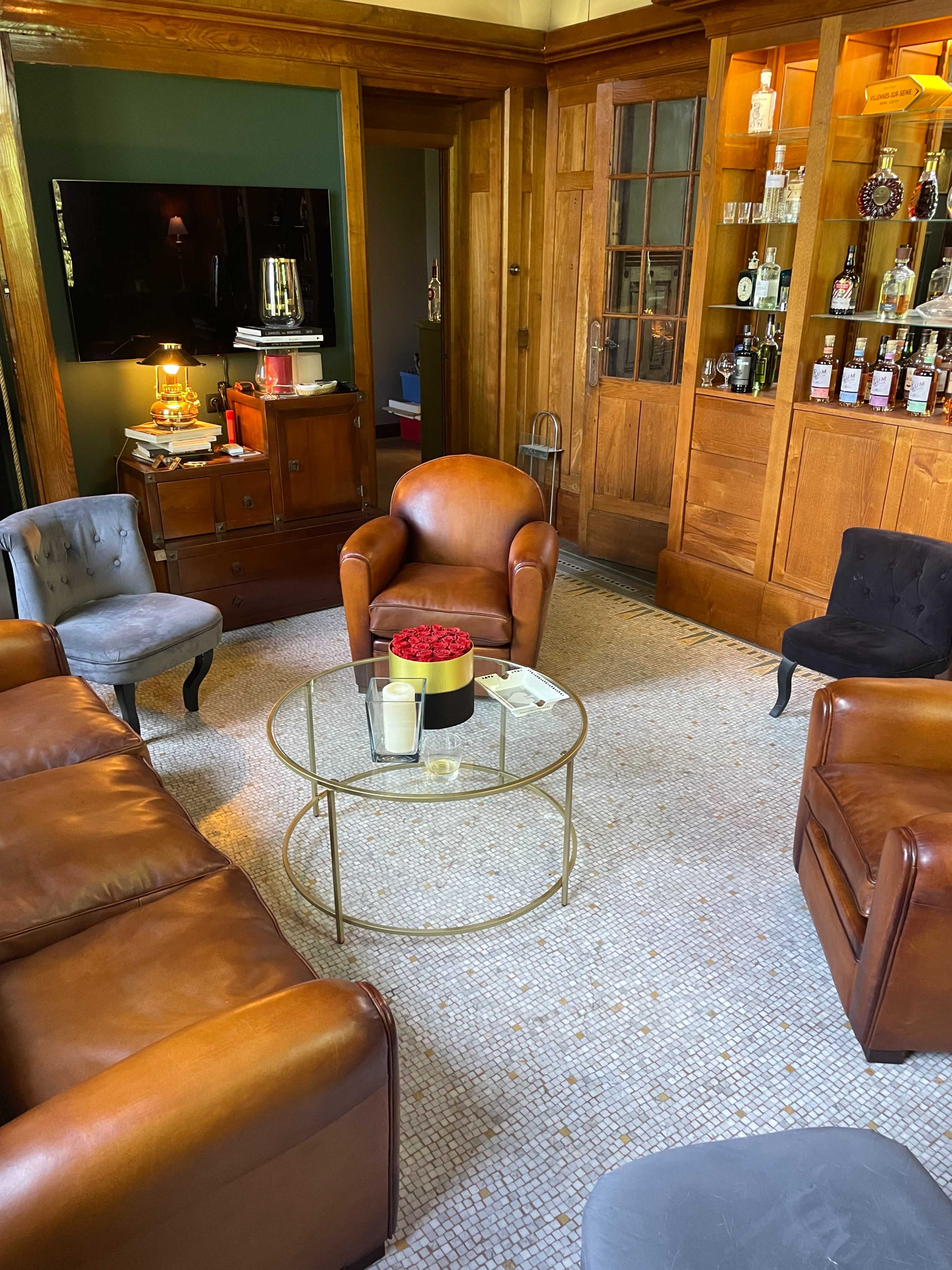 A living room featuring leather sofas, a round glass coffee table, and a wooden bar cabinet filled with glassware and bottles.