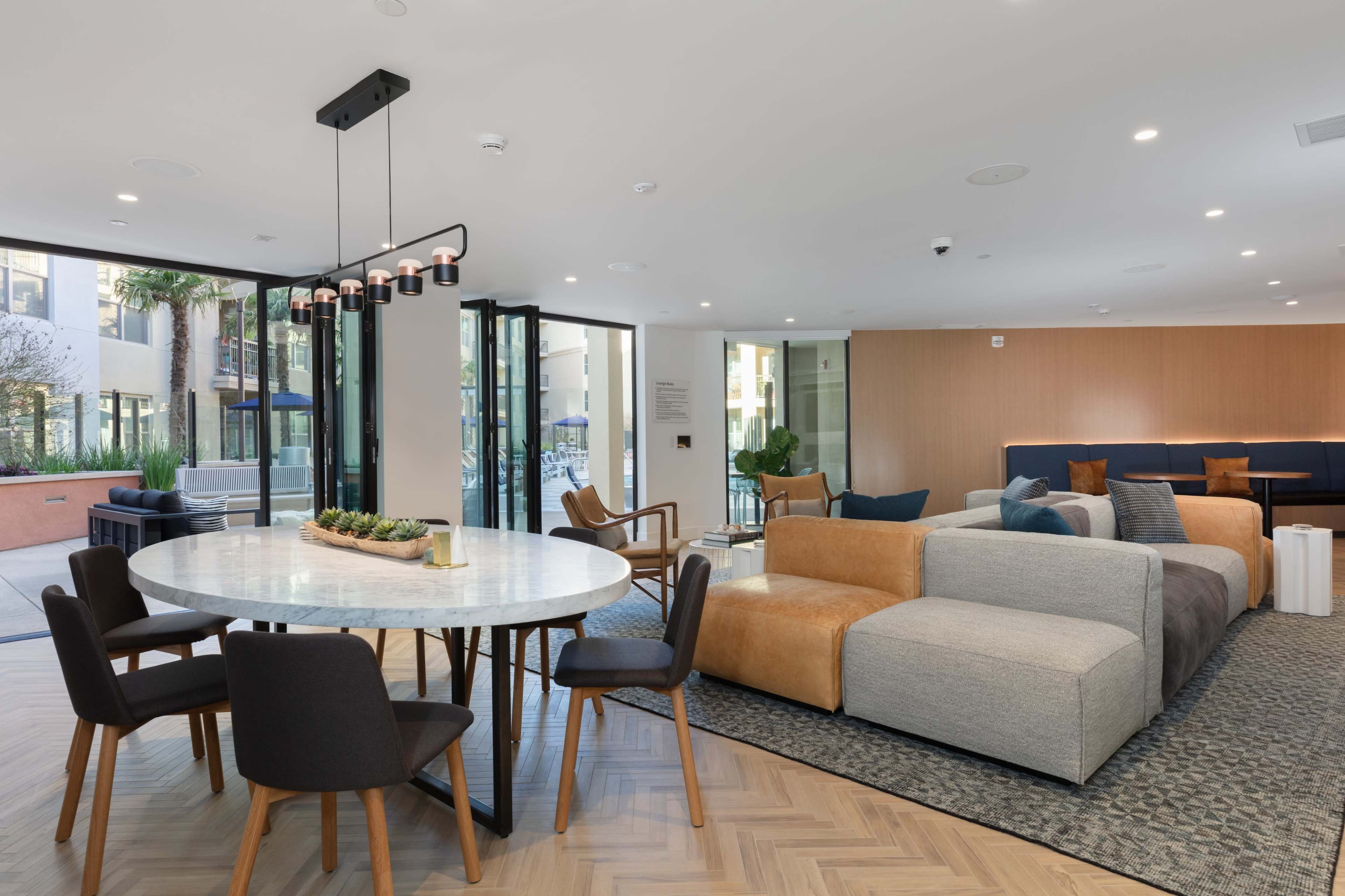 A modern interior space featuring a round dining table with chairs, a sectional sofa, and large glass doors that open to an outdoor area.