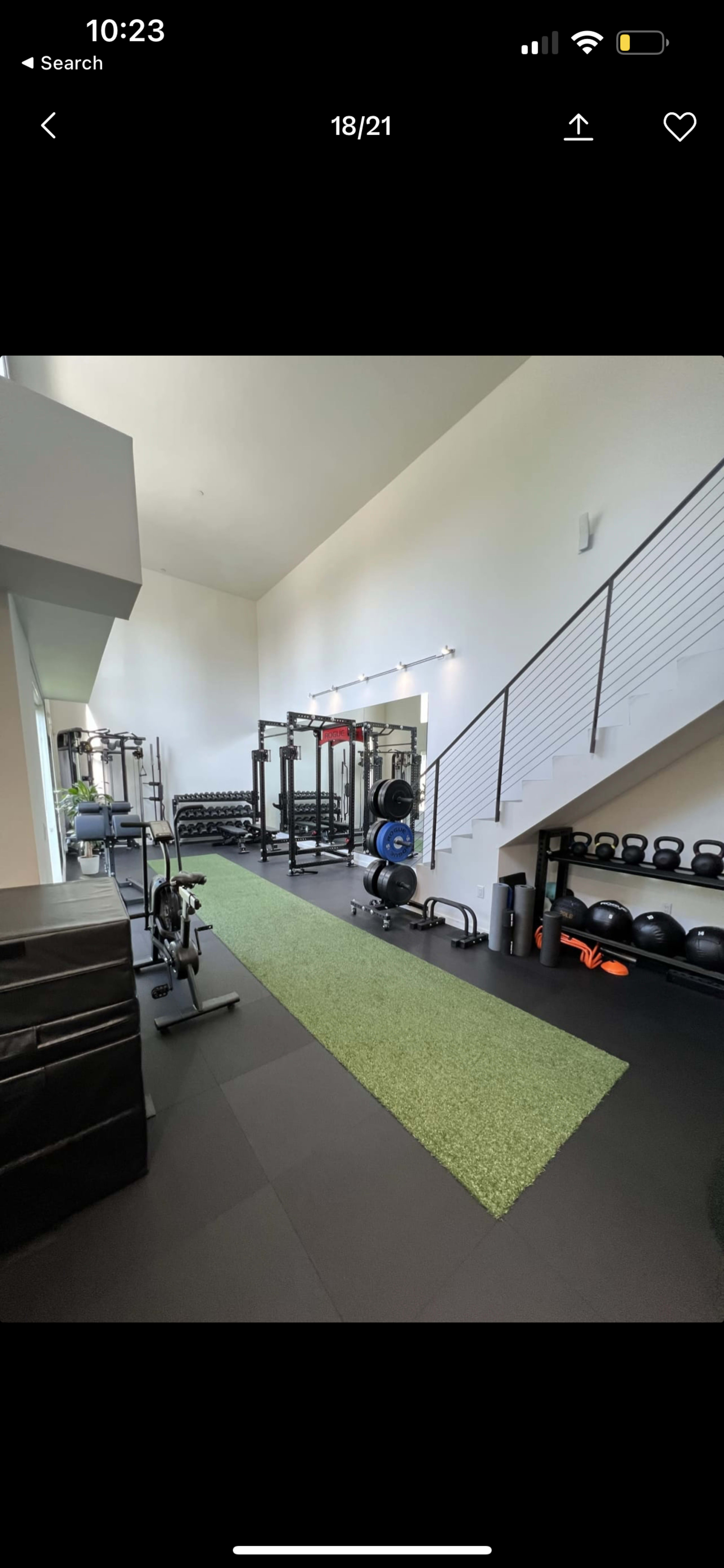 A spacious gym area featuring a variety of exercise equipment, including weights, a squat rack, and a green workout mat.