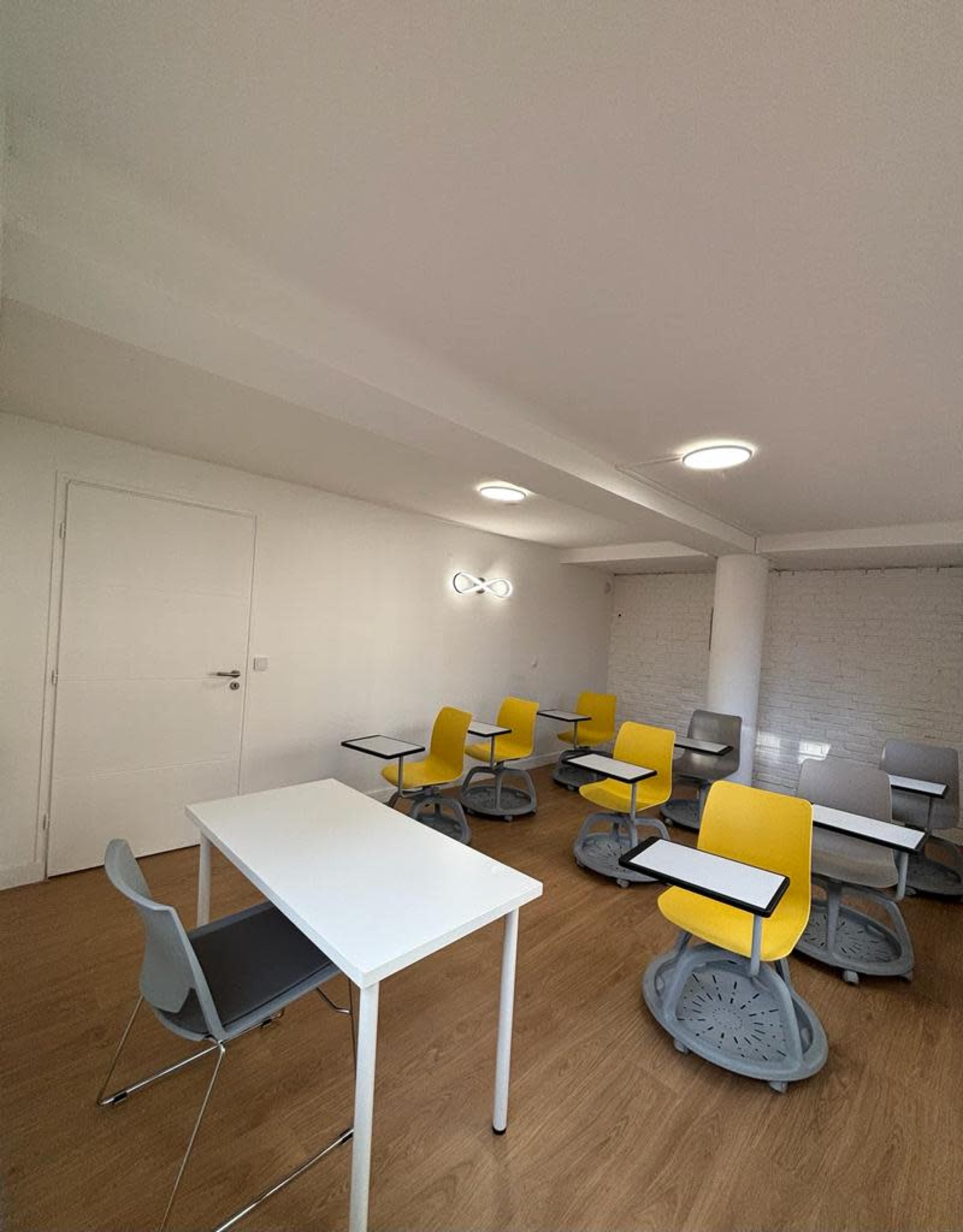 A brightly lit classroom with several yellow and gray chairs positioned around white tables.