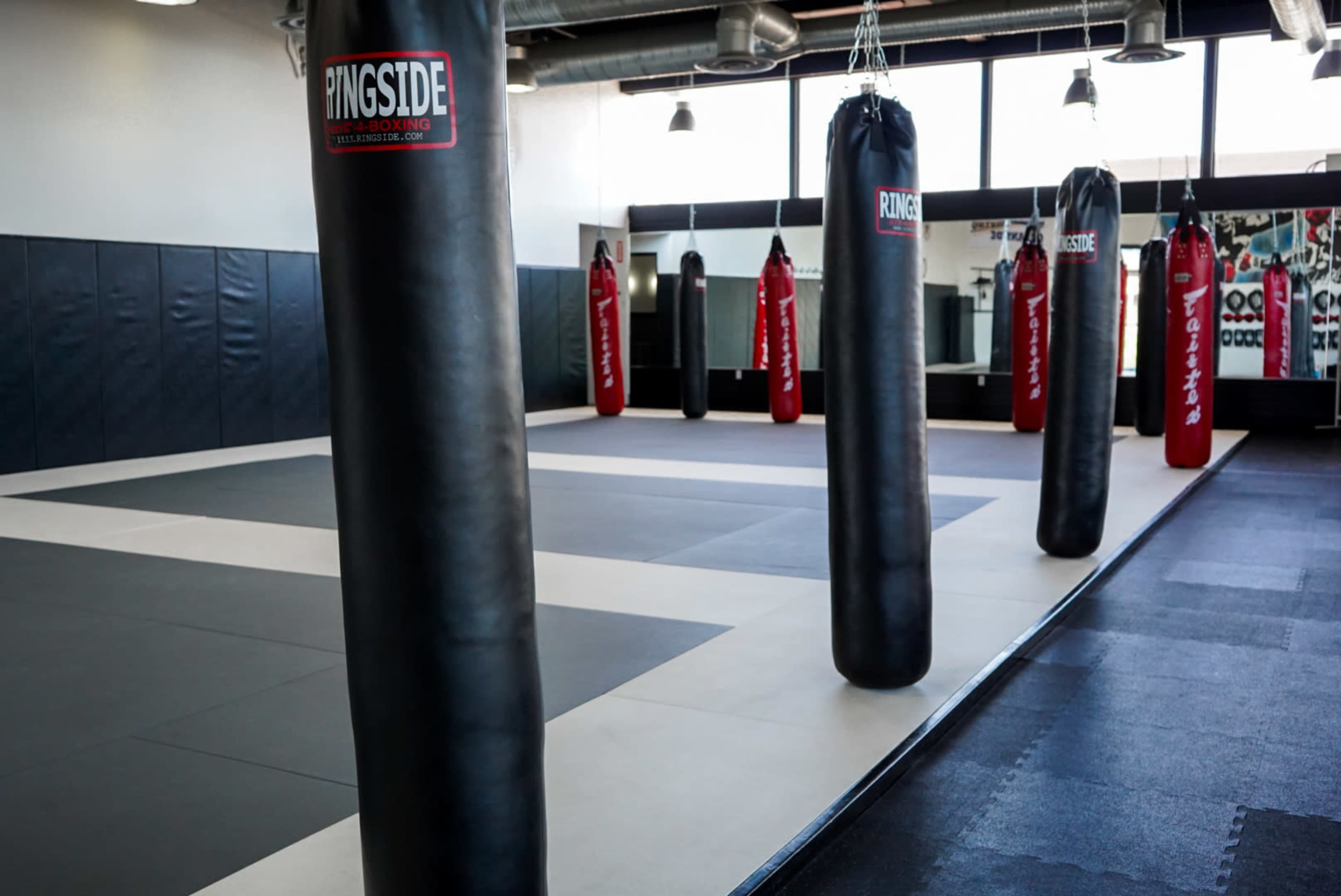 An empty boxing gym with several hanging black and red punching bags lined up against the walls.