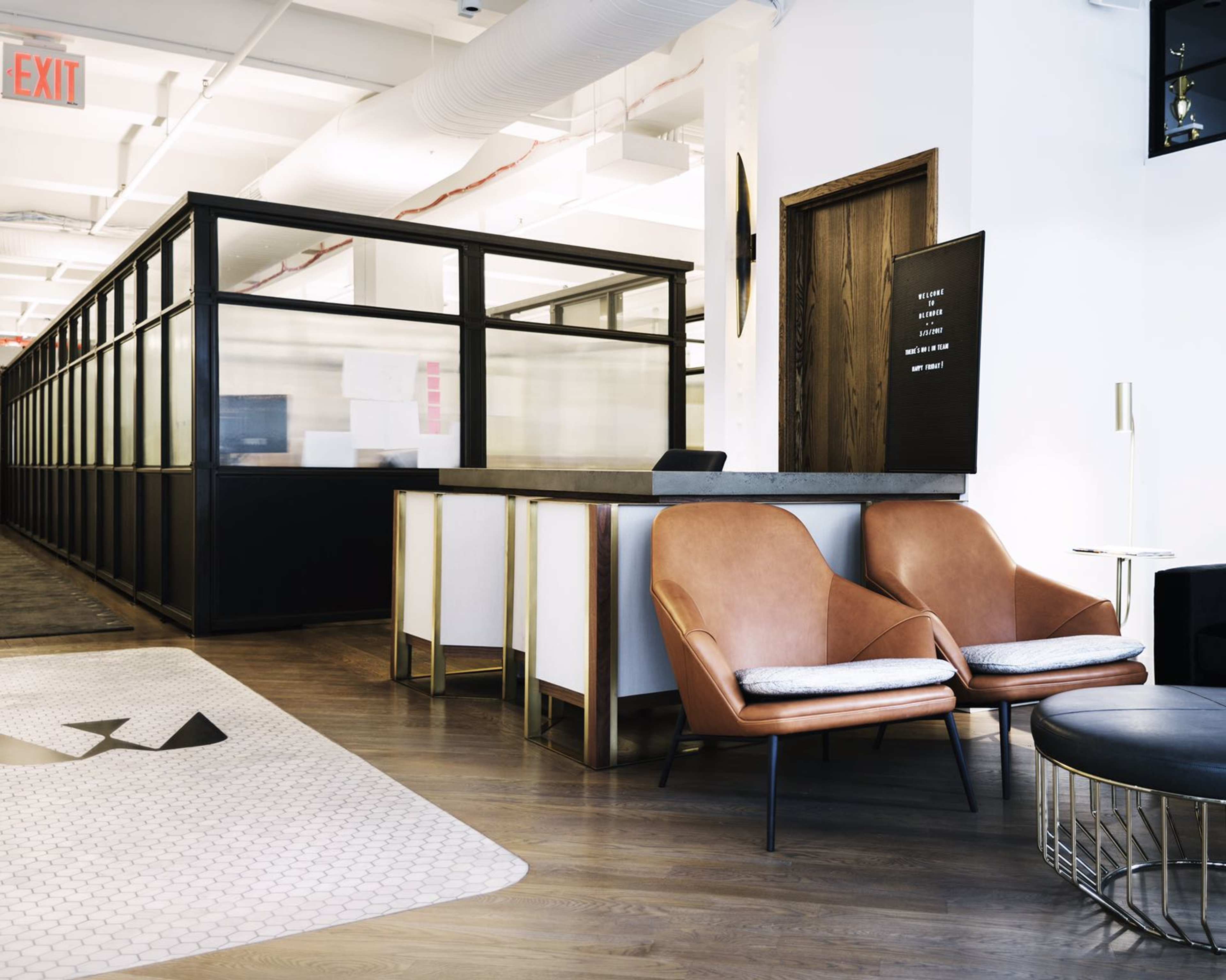 A modern office reception area featuring a desk, two stylish chairs, and a partitioned workspace in the background.