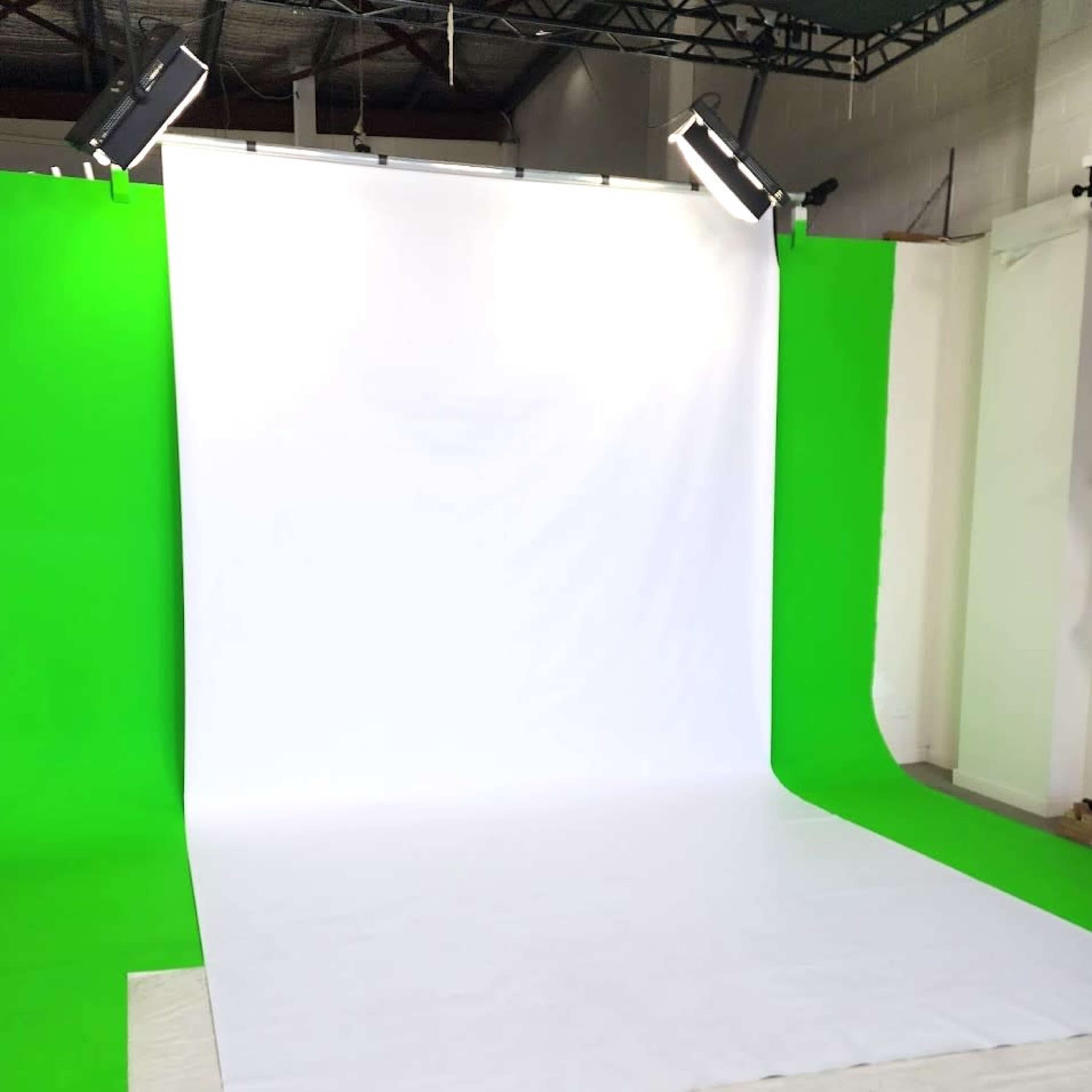 The image shows a photography studio setup with a white backdrop and green side panels illuminated by overhead lights.