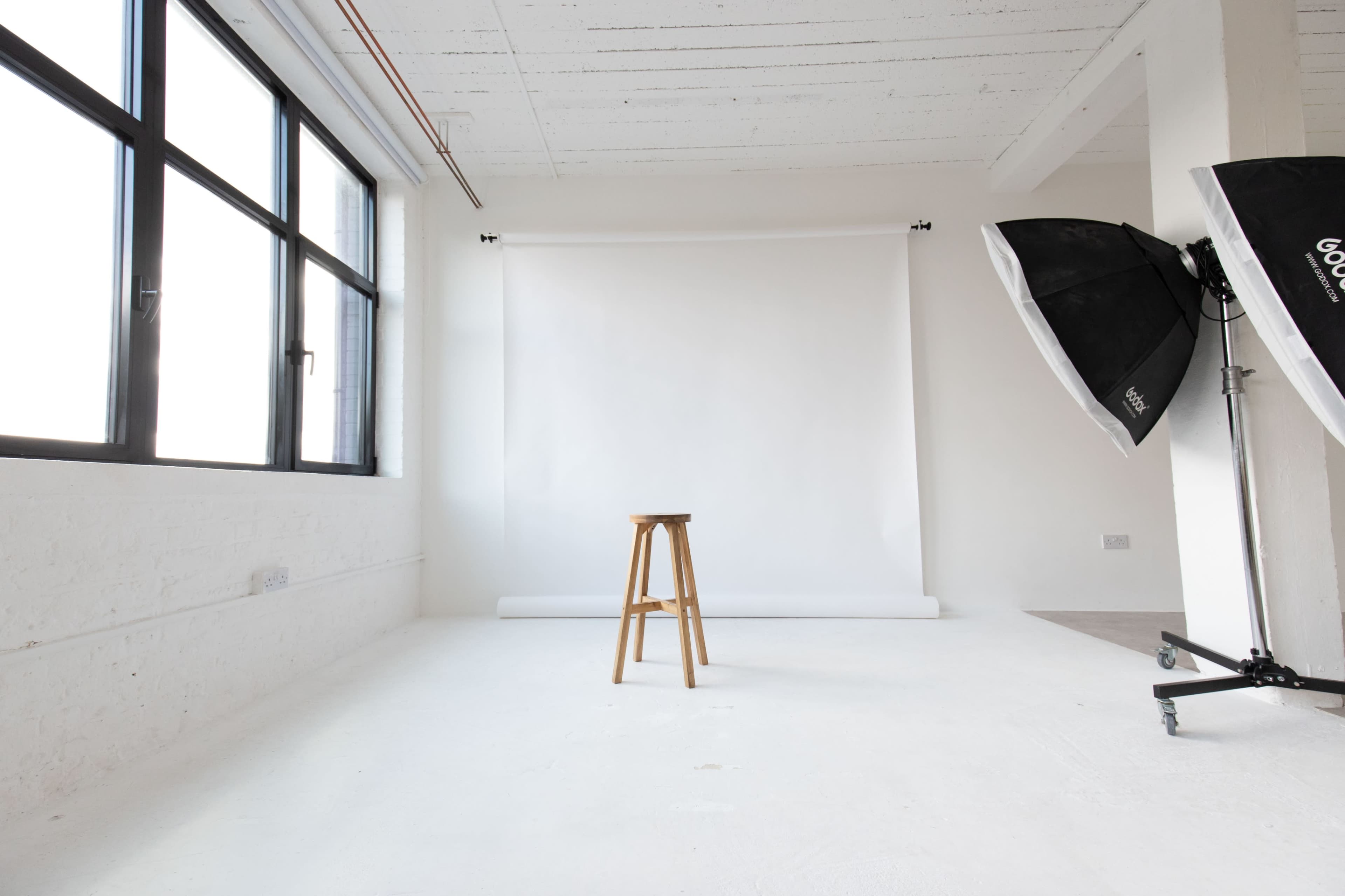A wooden stool is positioned in front of a white backdrop in a well-lit photography studio.
