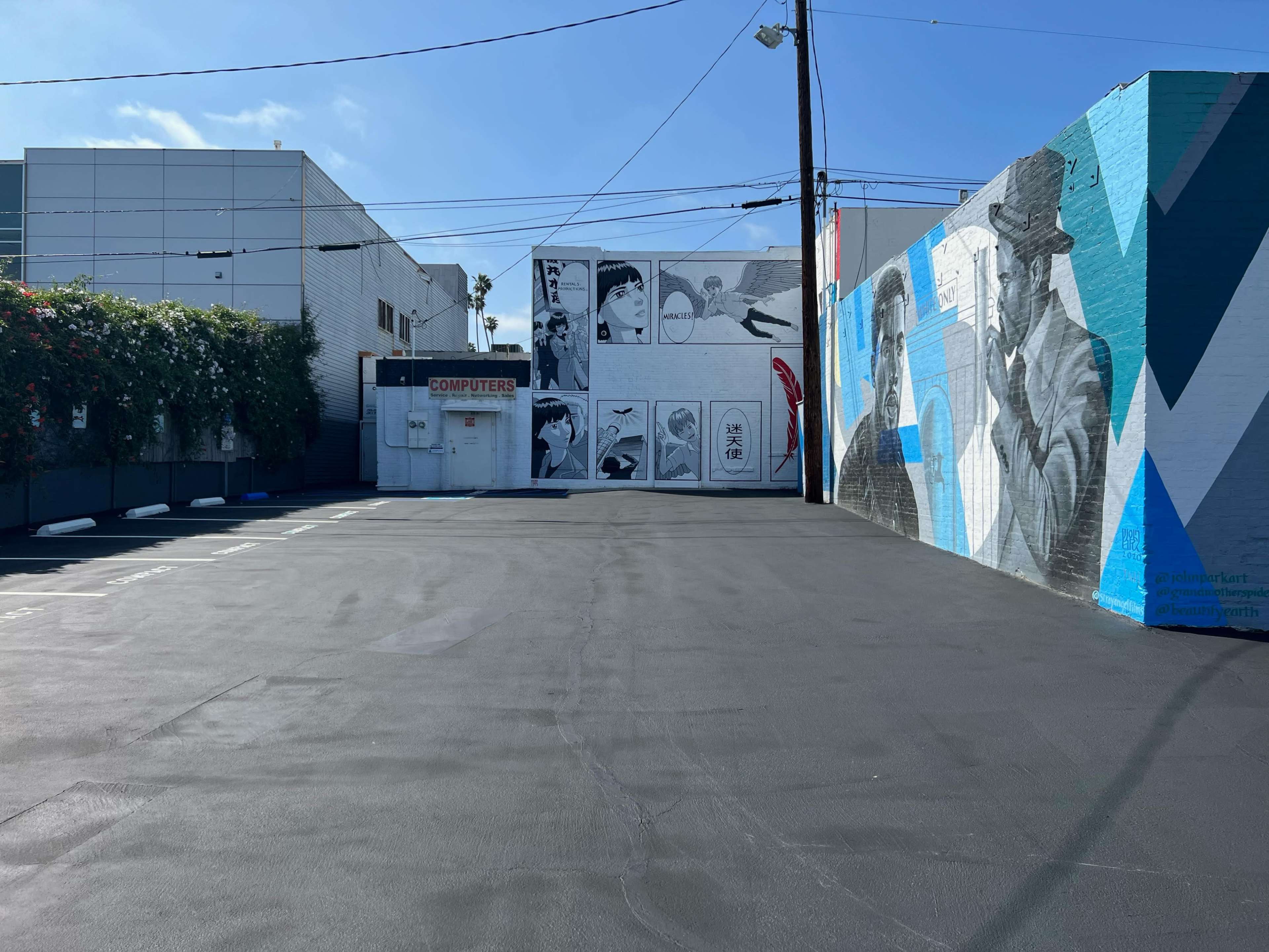 A street mural featuring black-and-white images of people on a wall, with a clear blue sky above and an empty parking lot in the foreground.