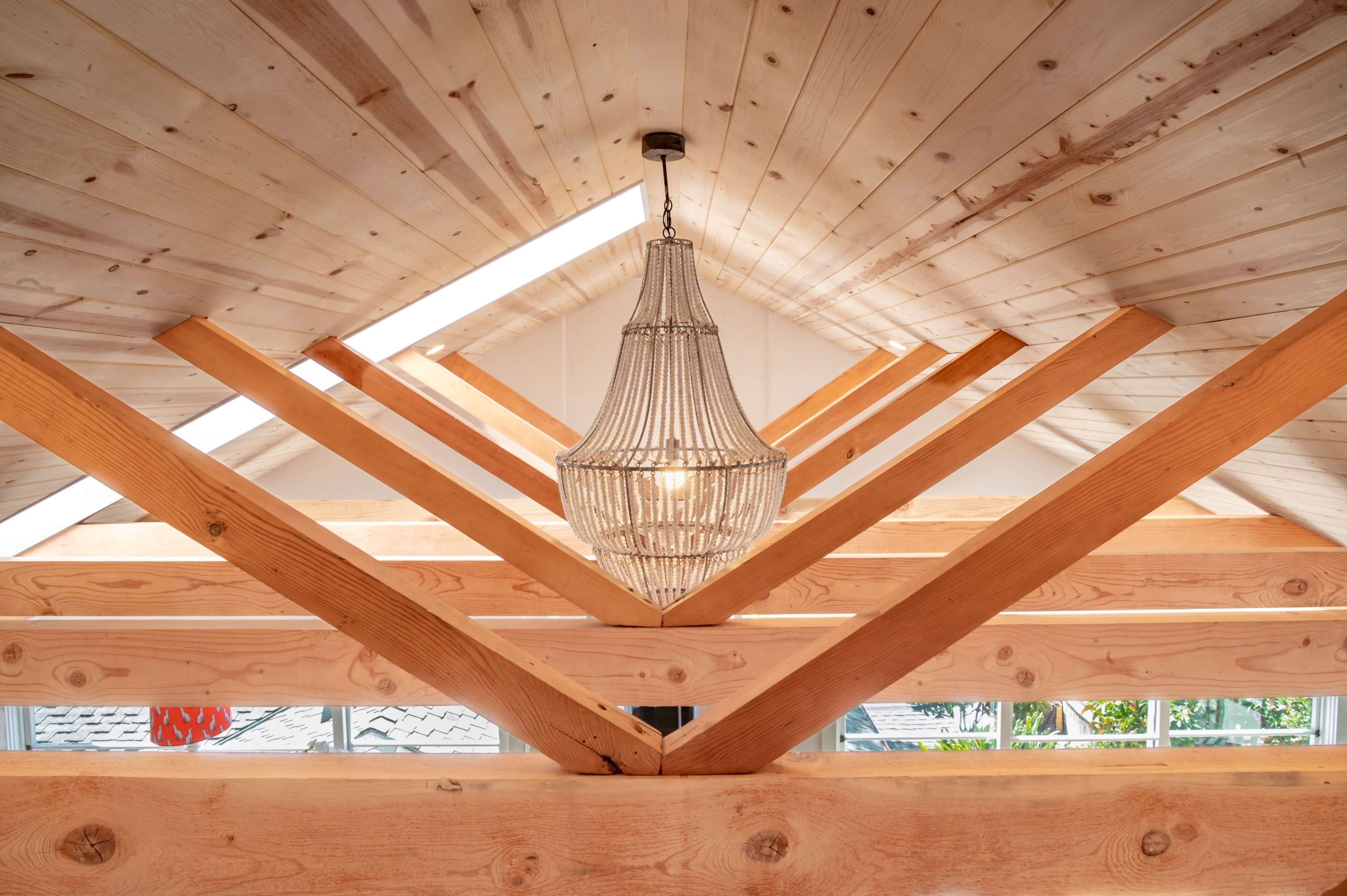 A wooden interior with exposed beams and a central chandelier hanging from the slanted ceiling.