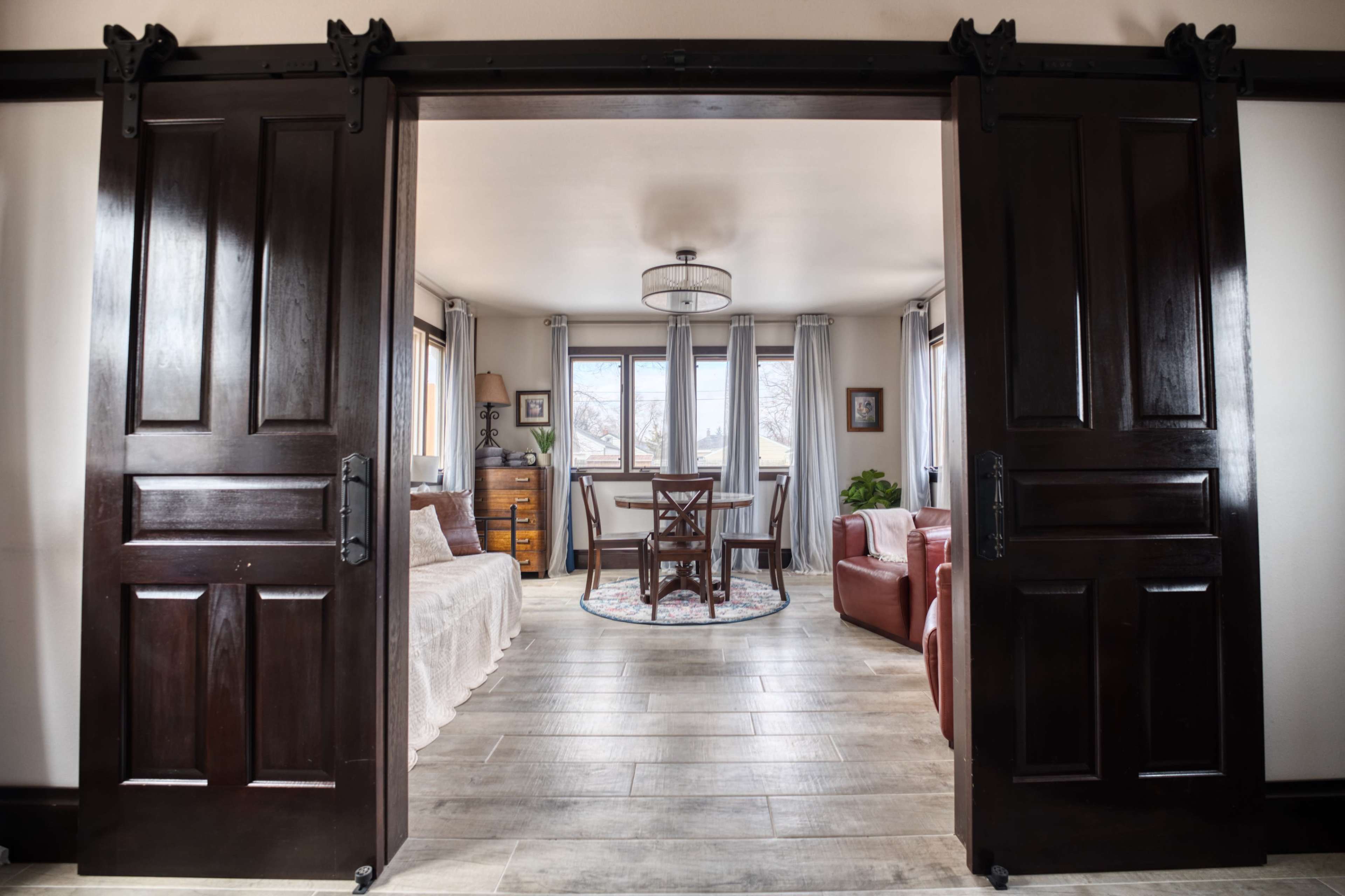 A doorway leading into a room with a dining table, chairs, a sofa, and large windows allowing natural light.