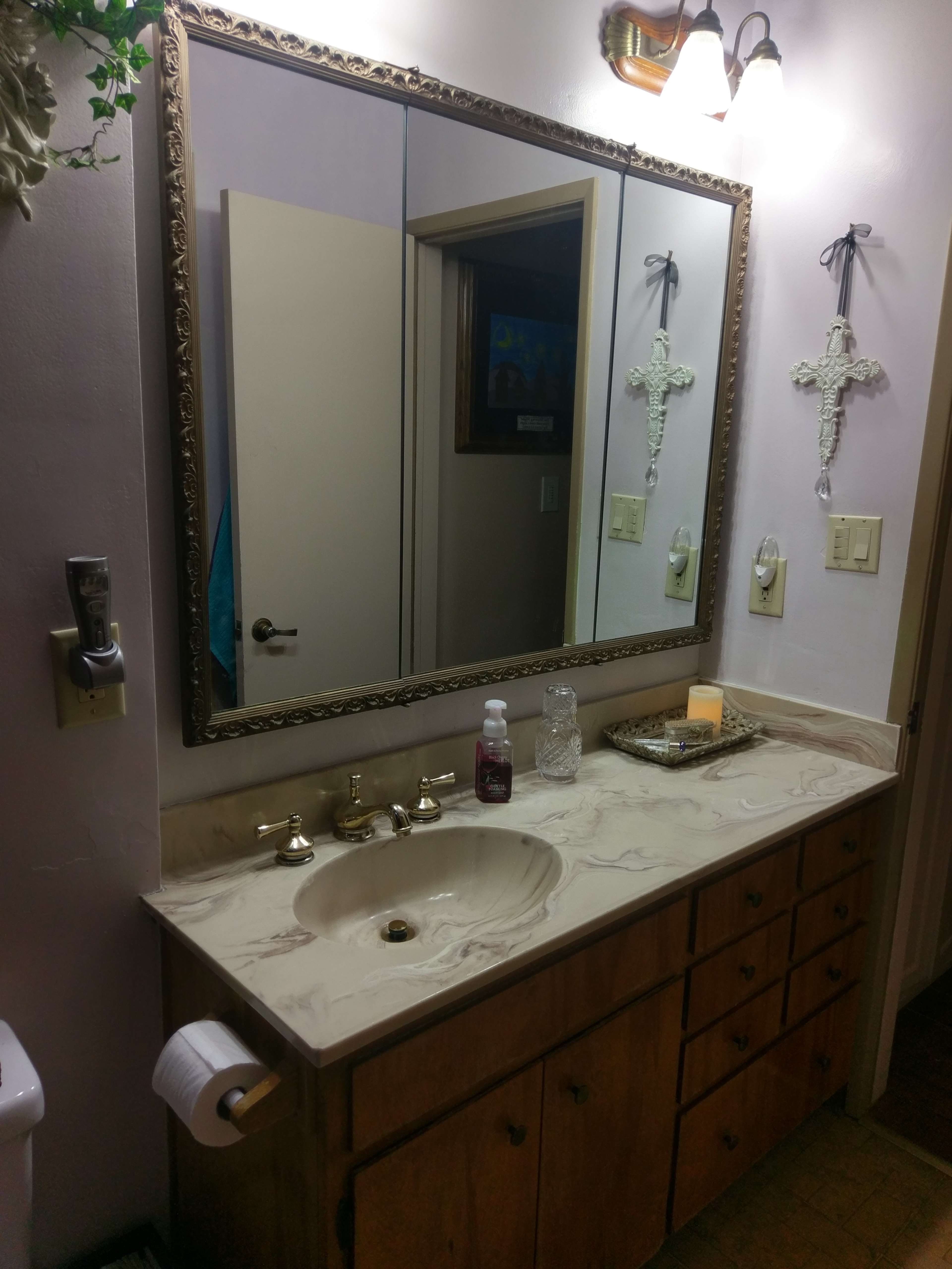 A bathroom vanity with a large mirror, a sink with a brass faucet, and wooden cabinets below, alongside decorative items on the countertop.