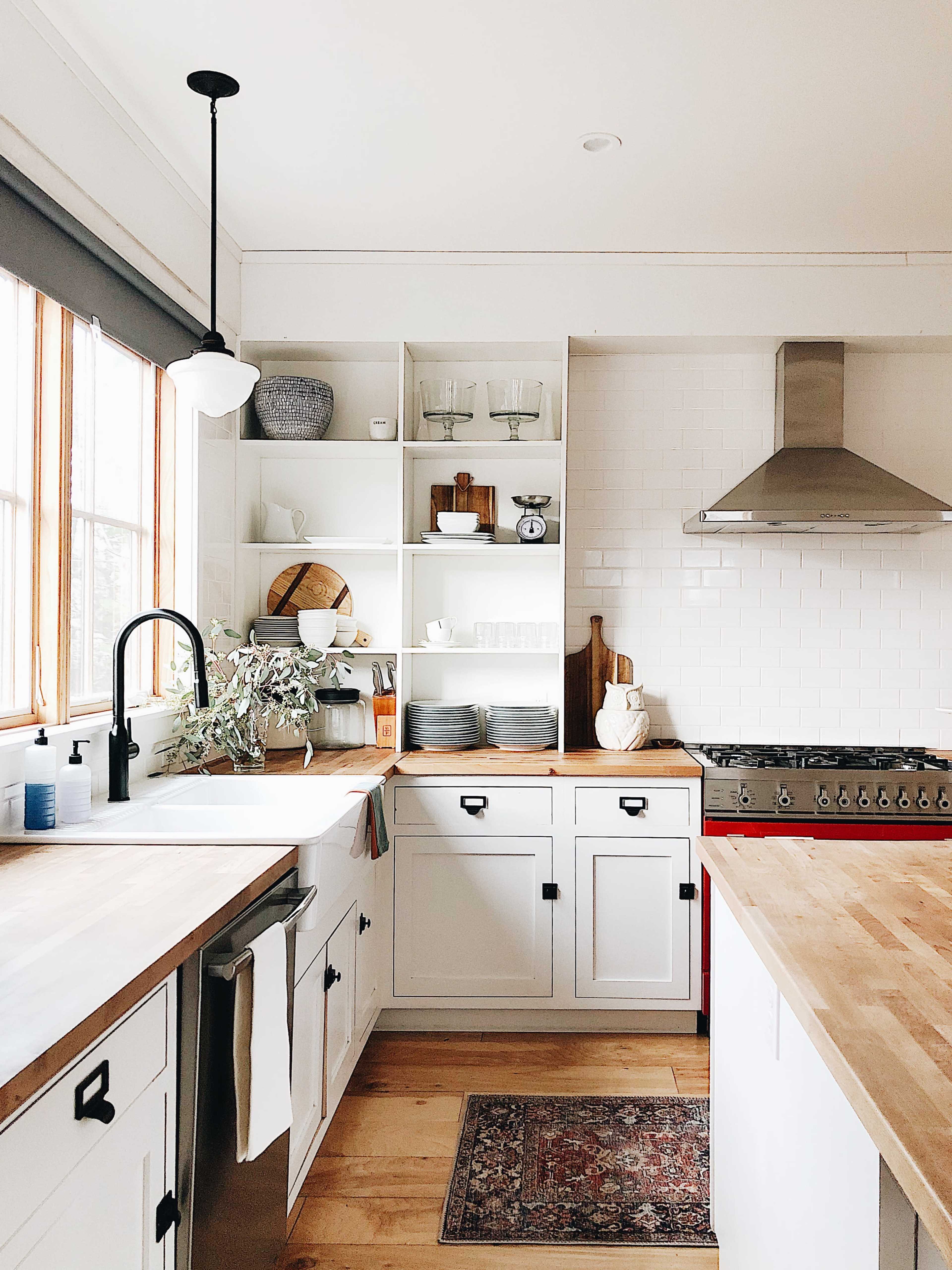 A modern kitchen with white cabinetry, open shelving displaying dishware, and a stainless steel stove.