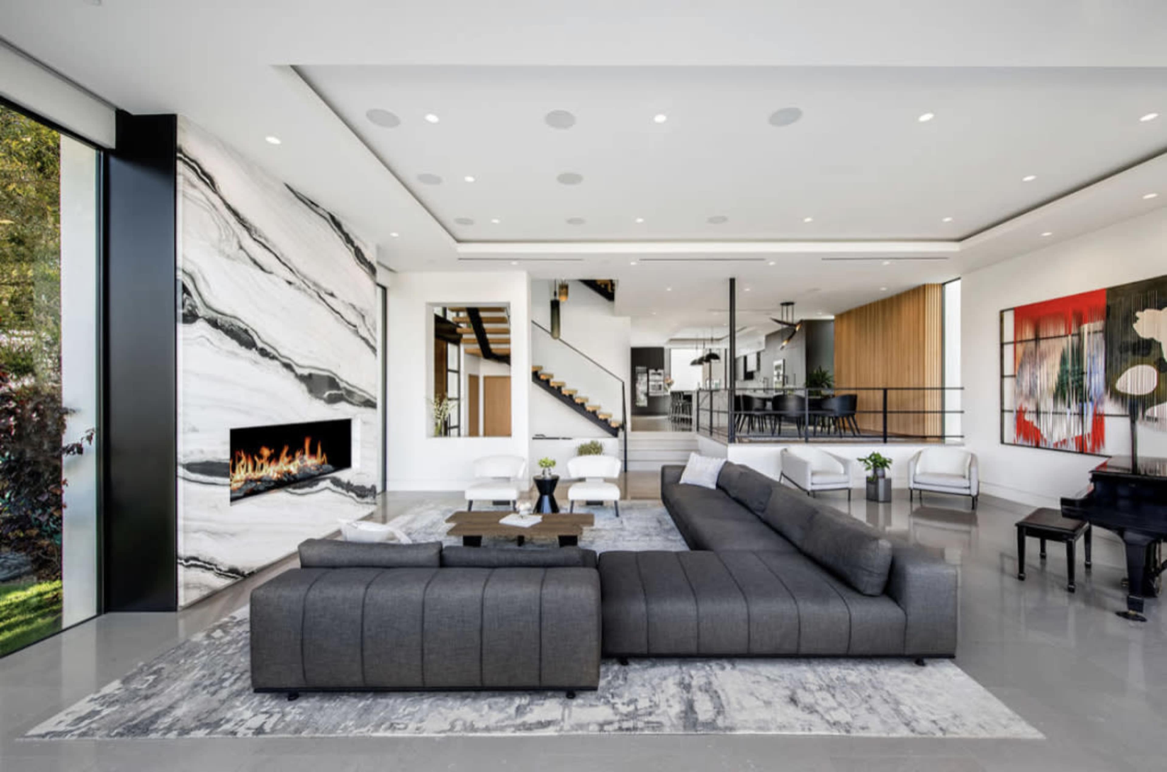 A modern living room features a large gray sectional sofa, a marble accent wall with a fireplace, and a view of an open dining area beyond.