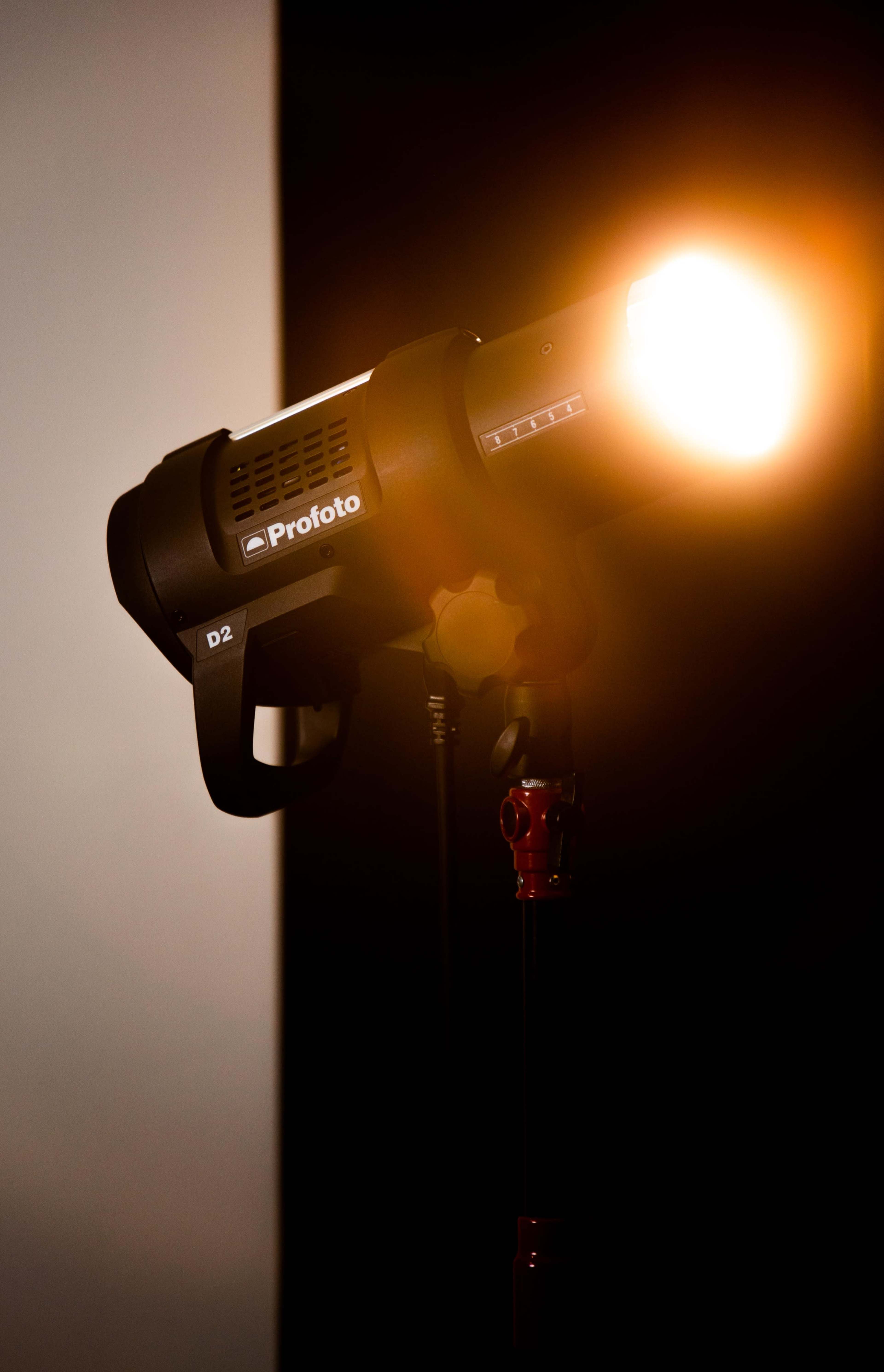 A studio light with a bright bulb is mounted on a light stand against a dark background.