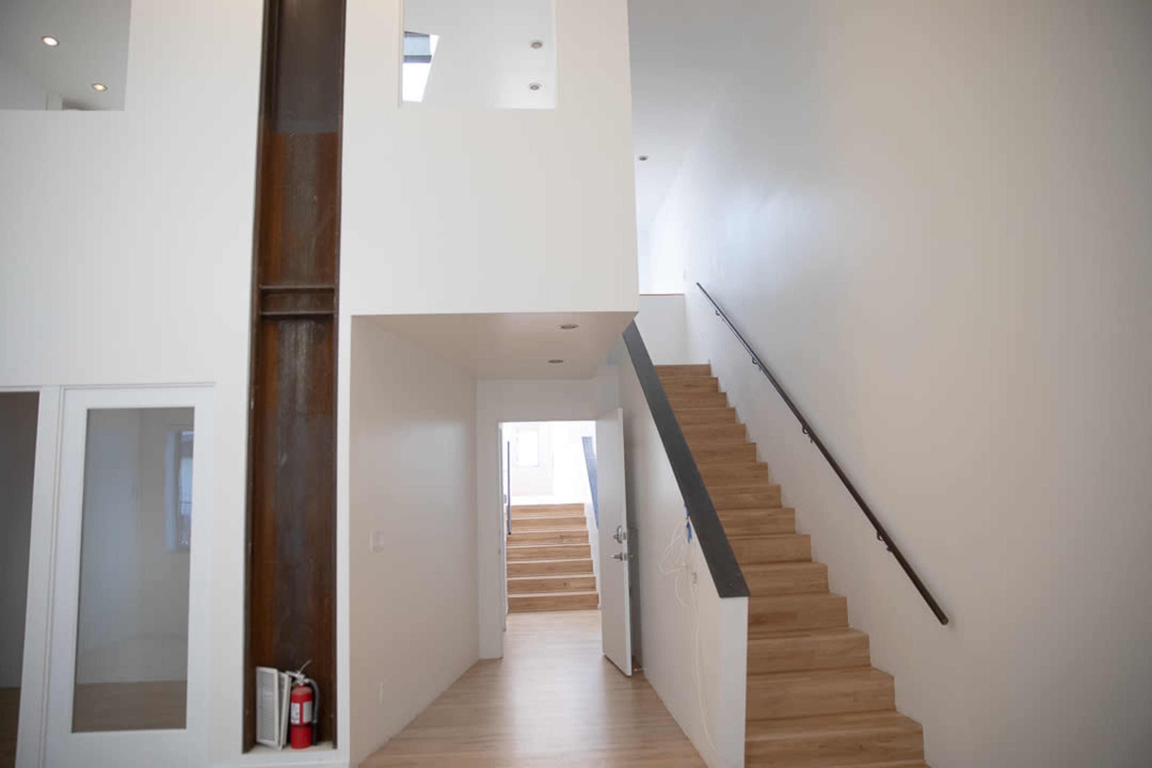 A modern interior space featuring a staircase with wooden steps, white walls, and large windows that allow natural light to enter.