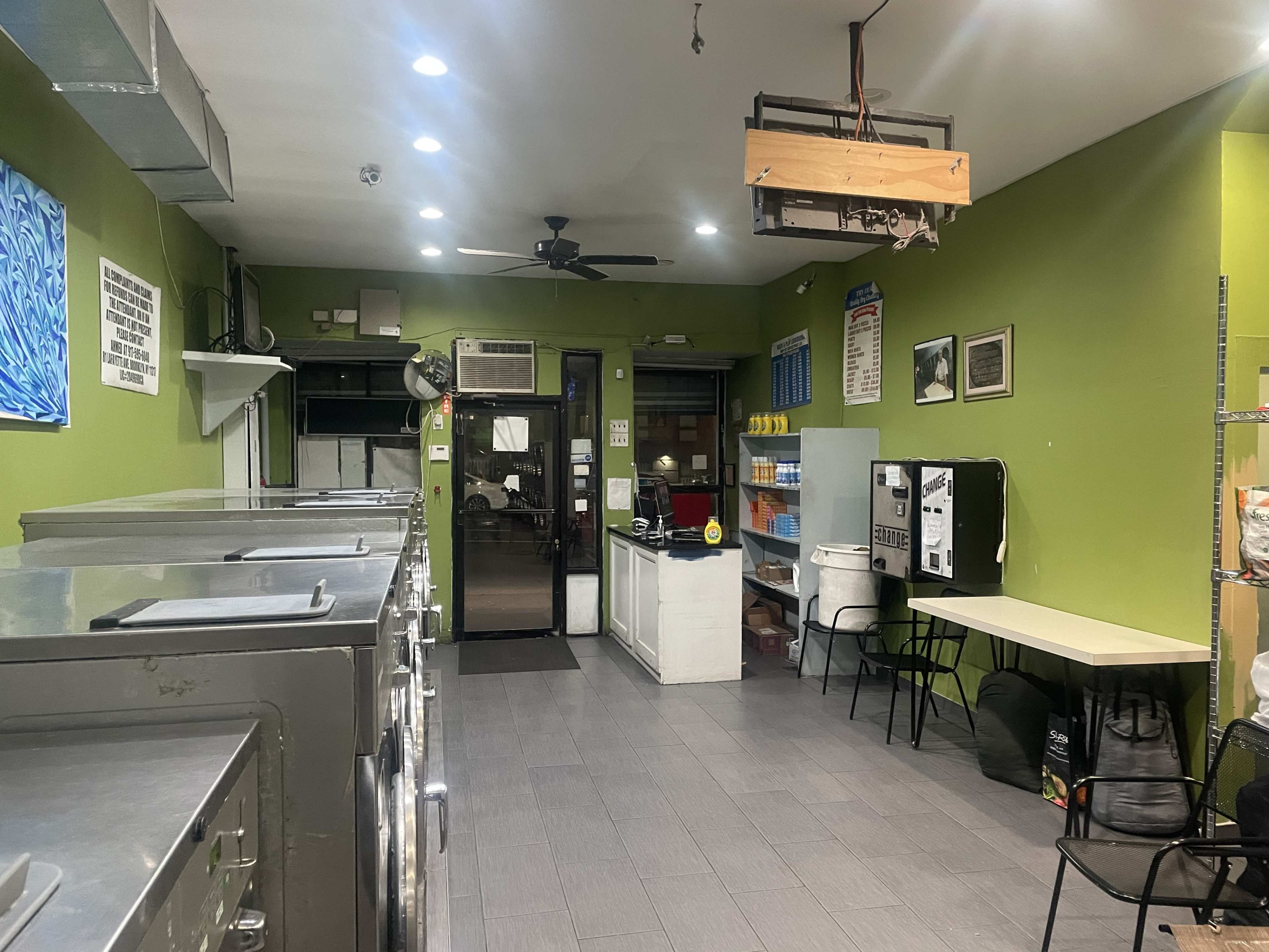 A laundry room with several washing machines on one side, a service counter, and seating against a green wall.
