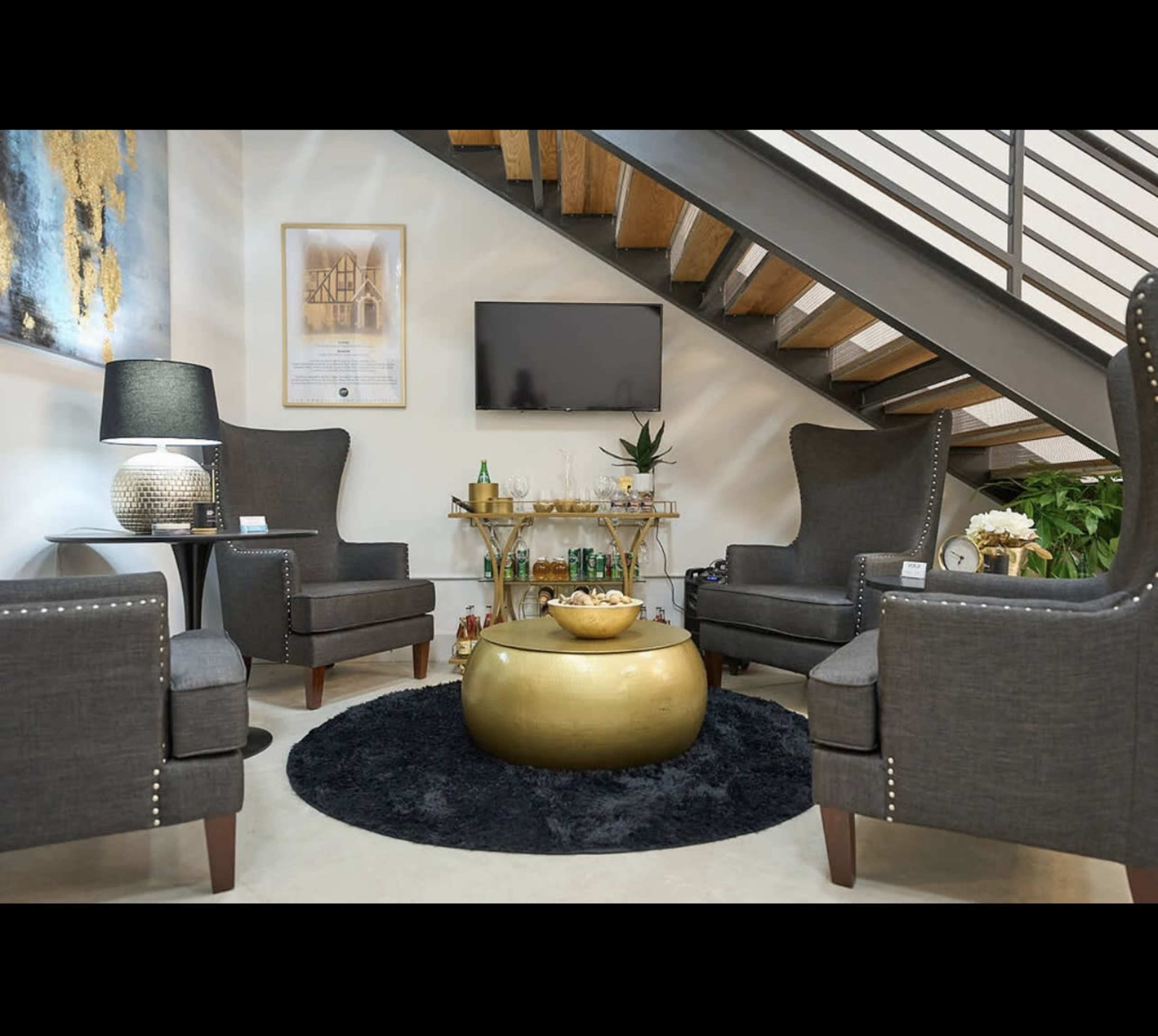 A cozy seating area features three upholstered chairs, a decorative table, and a television, all situated beneath a staircase.