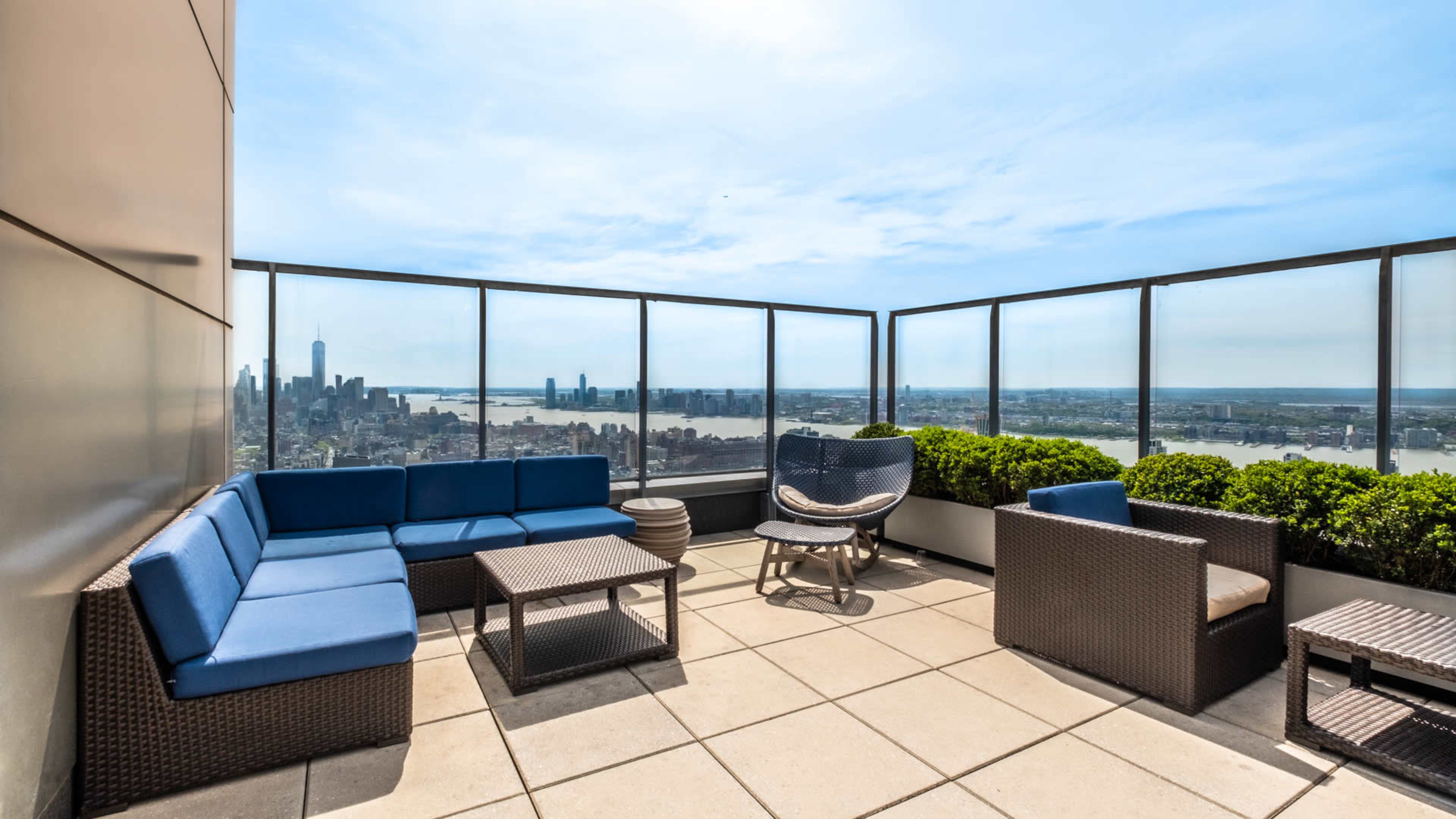 A rooftop terrace with blue seating, a small table, and a view of a city skyline and river.