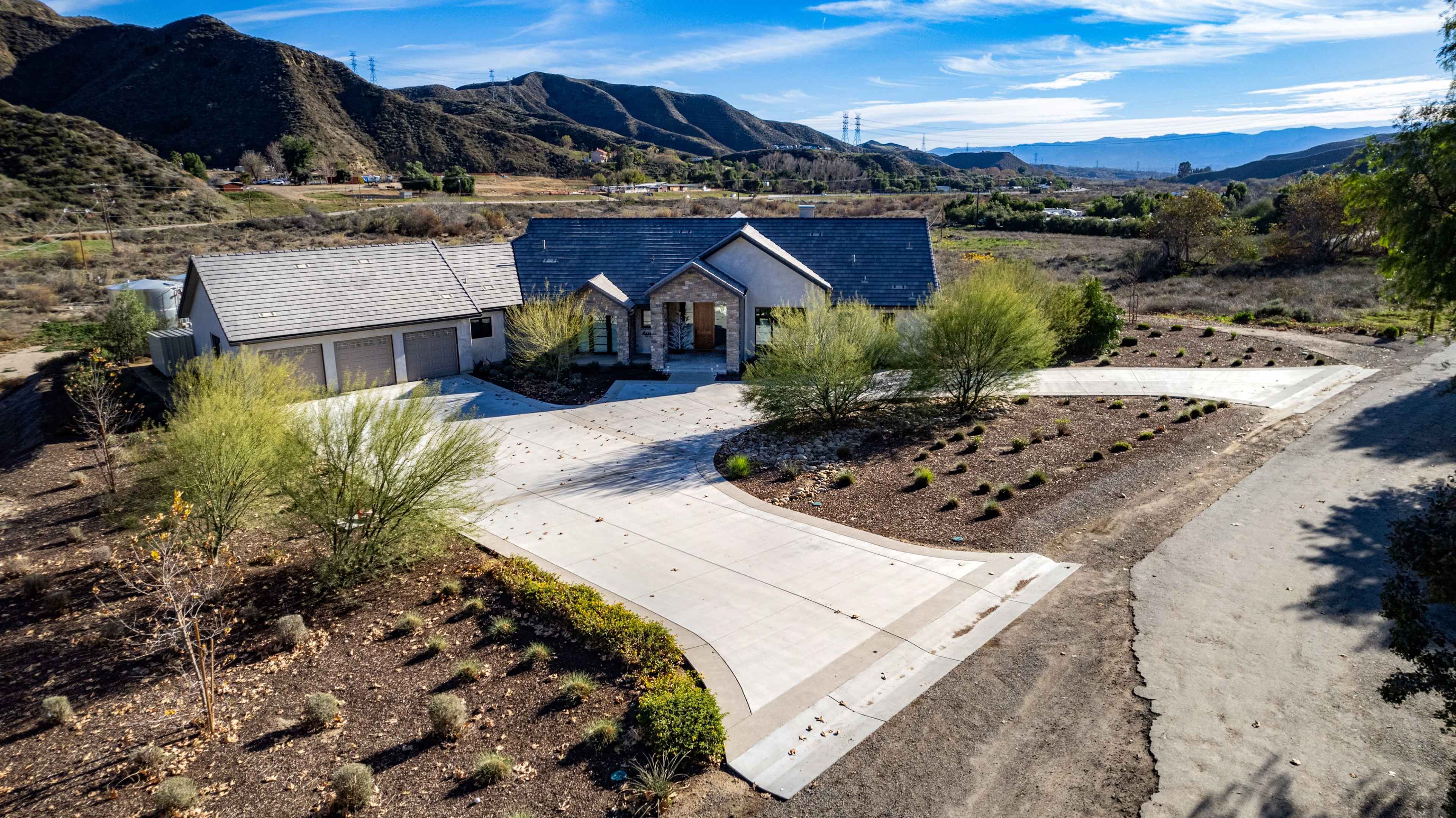 A modern house situated on a hillside with a large driveway and surrounding landscaping in a rural area.