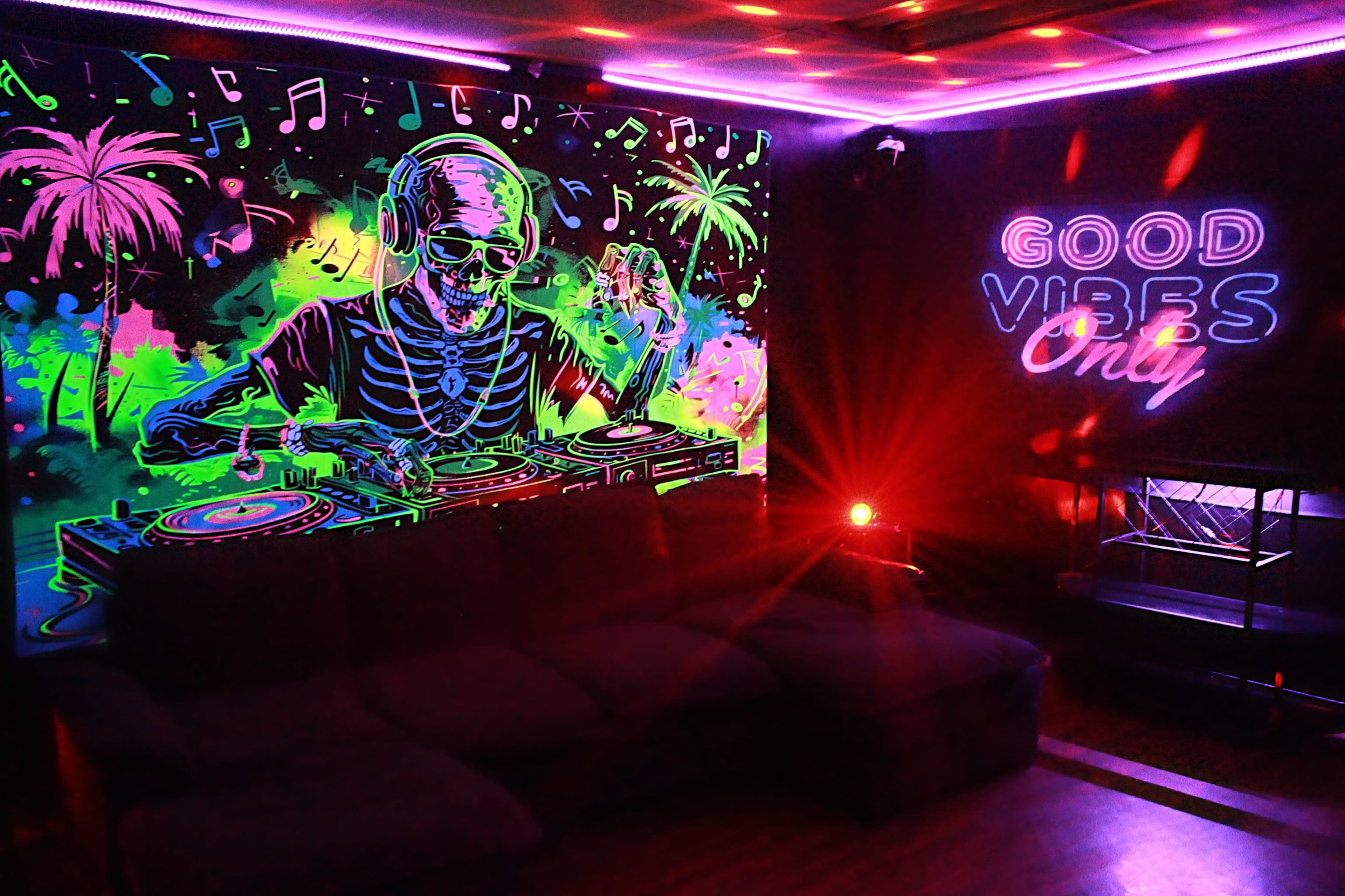 The image features a vibrant, neon-lit room with a skeleton DJ mixing music next to a glowing "GOOD VIBES ONLY" sign.
