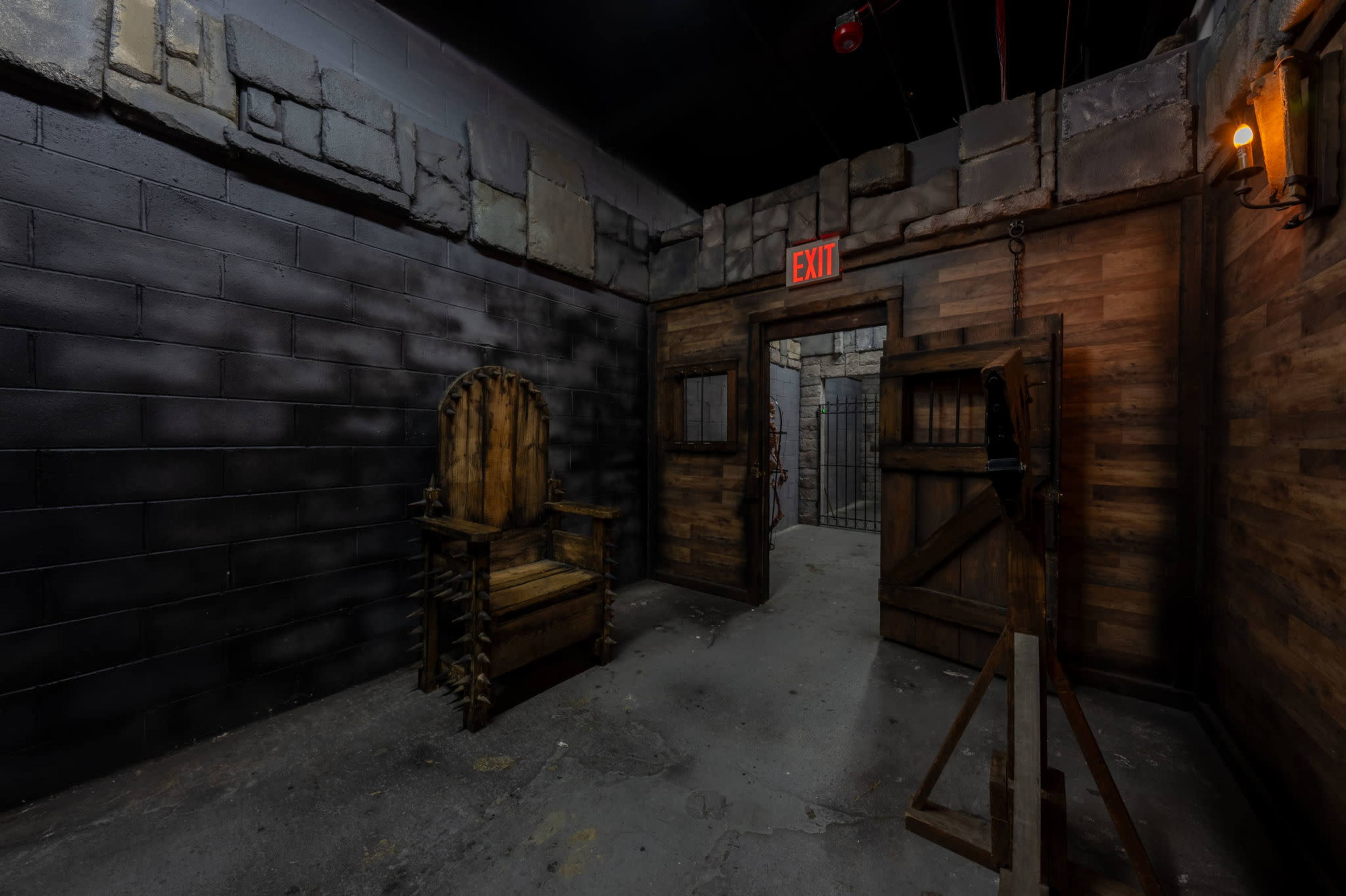 The image depicts a dimly lit room with stone and wooden walls, featuring a throne-like chair, an exit sign, and a doorway leading to another area.
