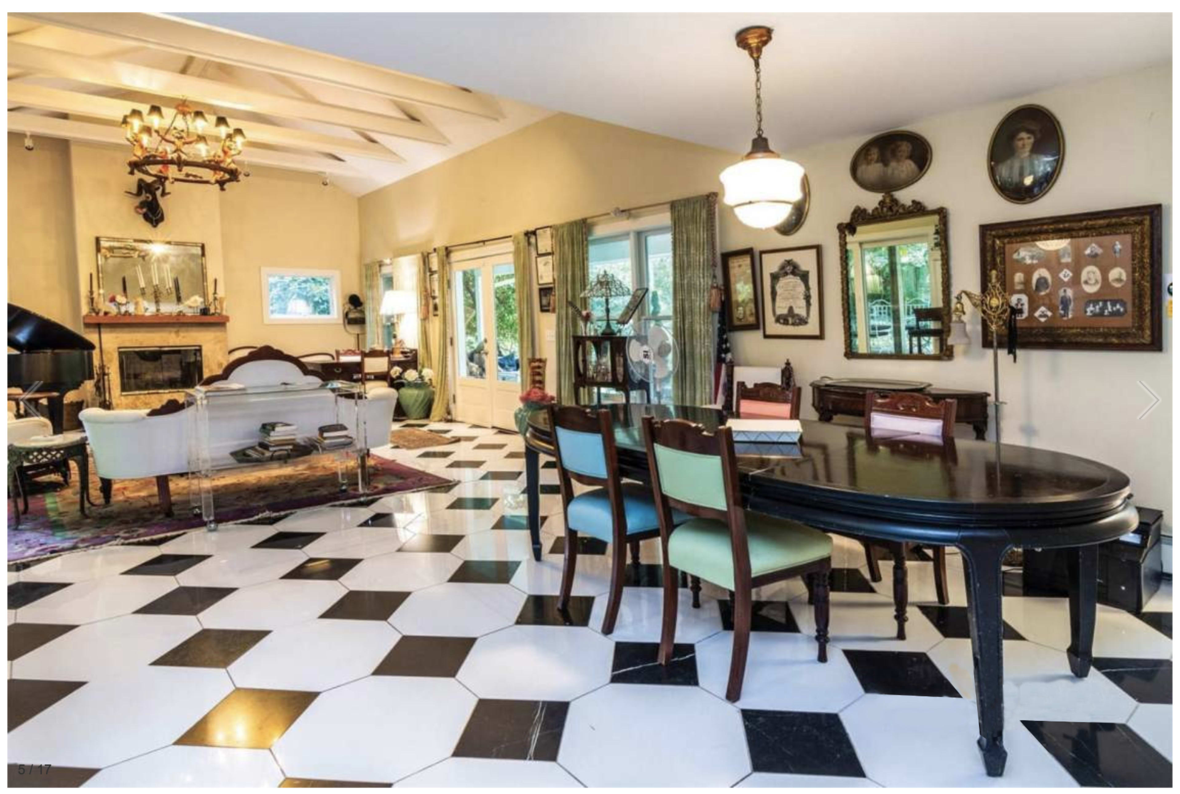 A spacious dining area with a black-and-white checkered floor, a round dining table surrounded by chairs, and various framed pictures and decorative items on the walls.