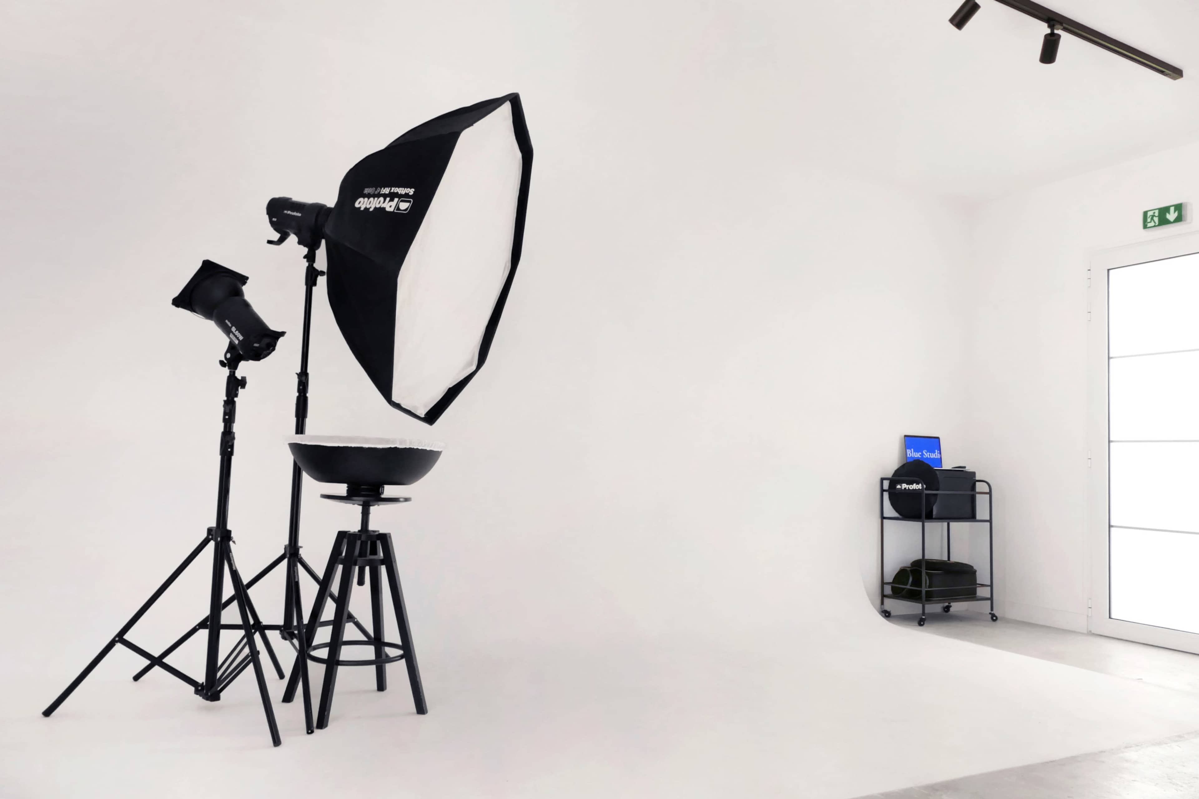 A photography studio with lighting equipment, a black stool, and a rolling cart against a plain white backdrop.