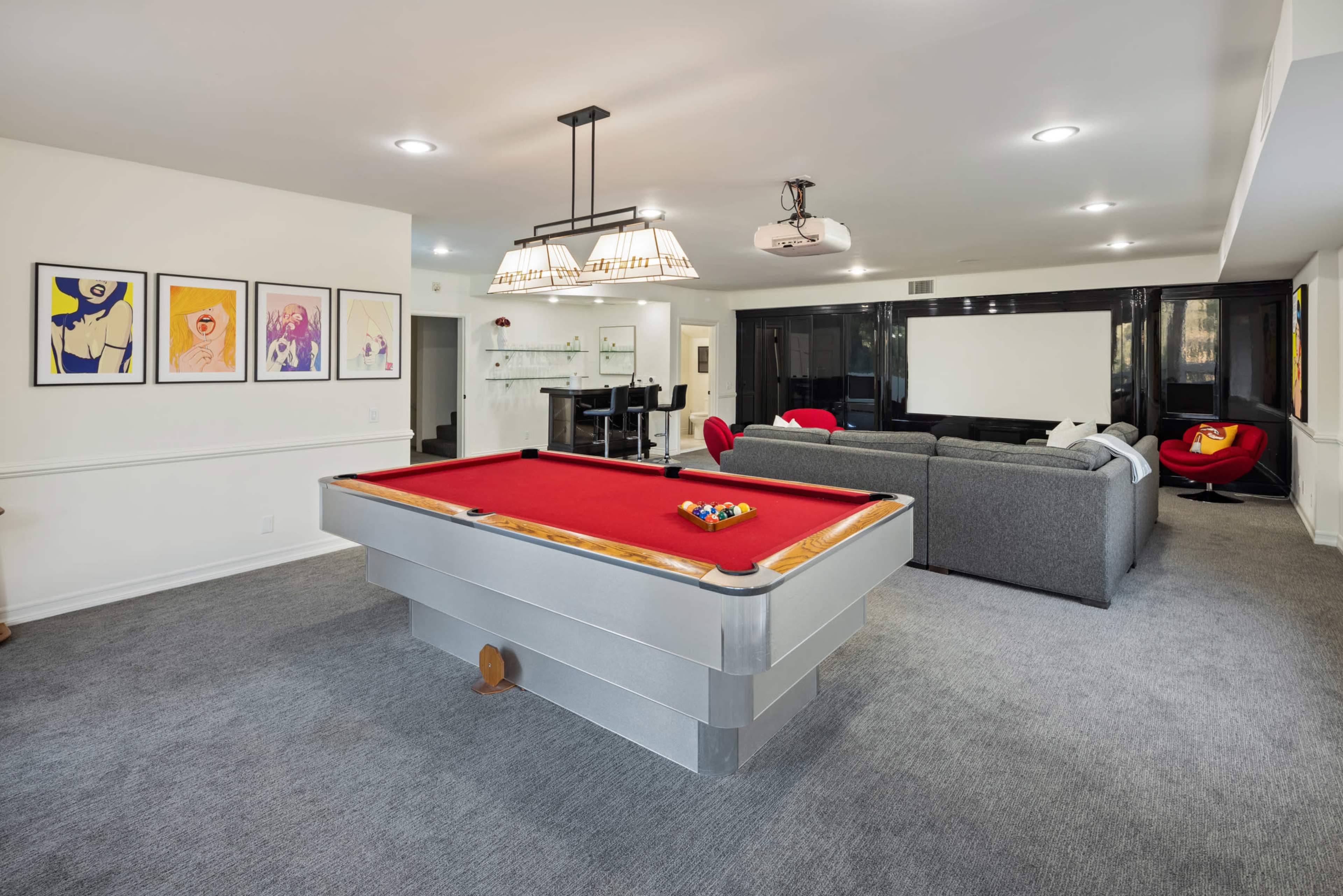 A modern game room featuring a red pool table in the center, surrounded by a stylish seating area and framed artwork on the walls.