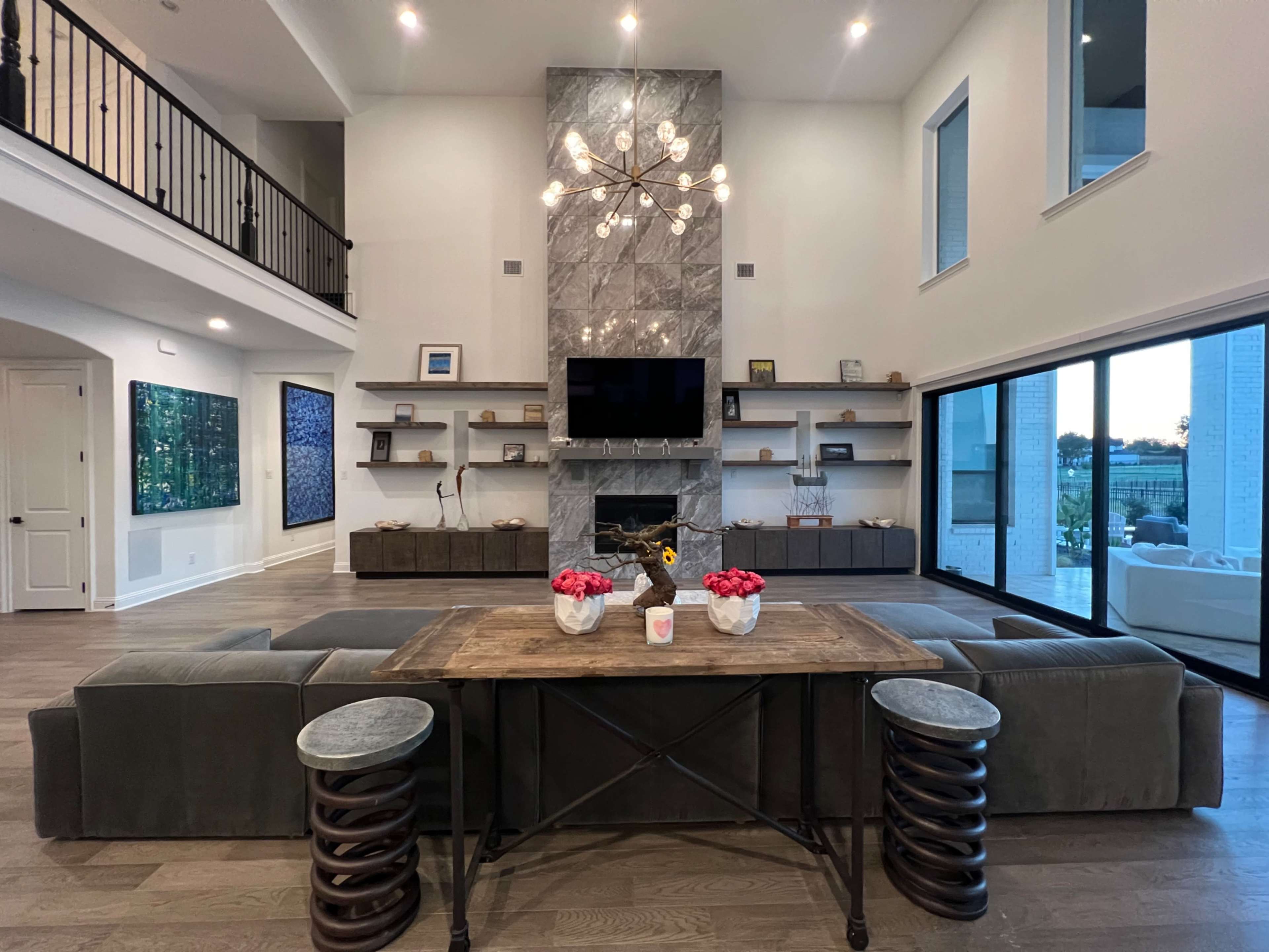 The spacious living room features a large seating area centered around a coffee table, with a modern stone fireplace and shelves in the background.