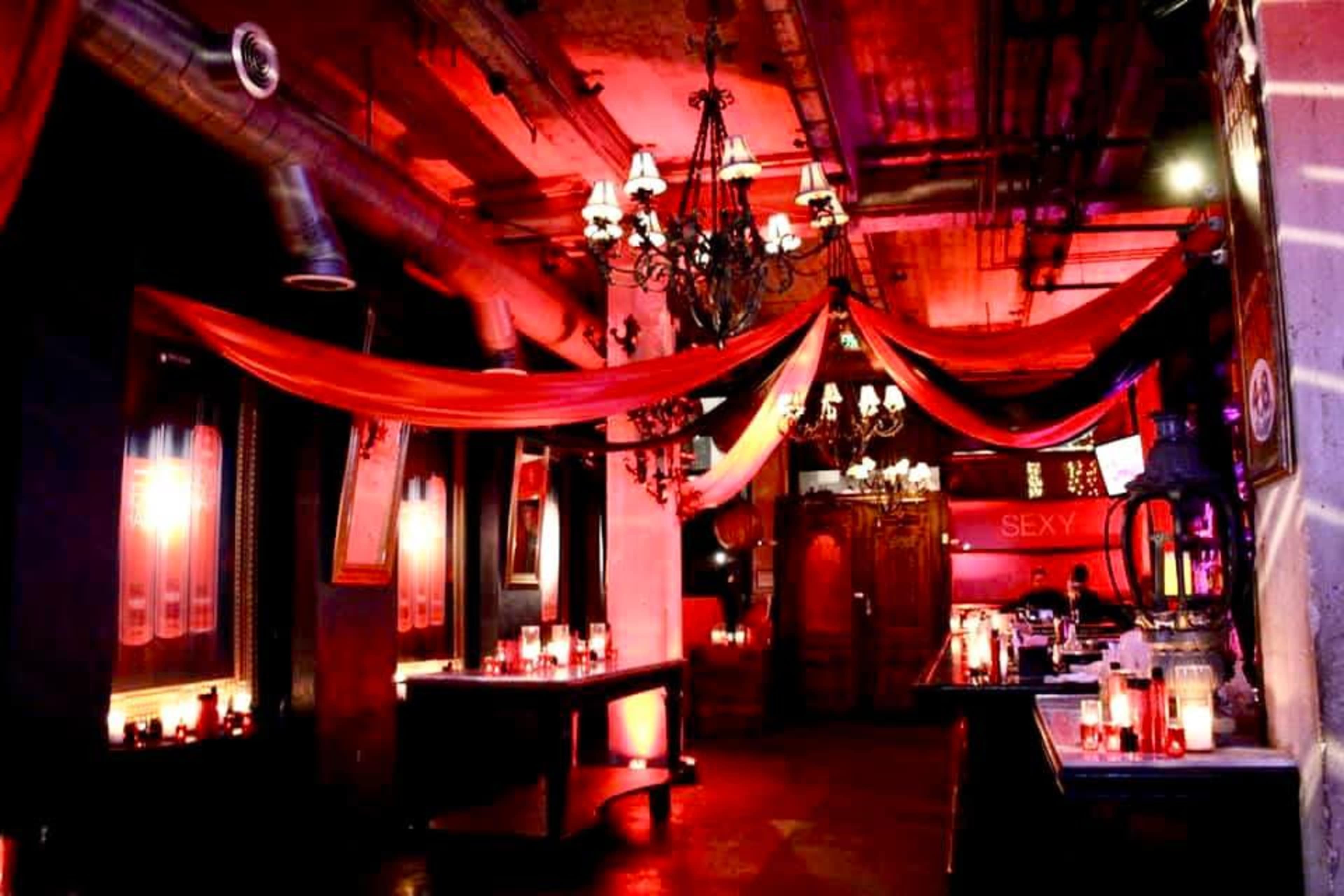 A dimly lit bar interior decorated with red fabric draped from the ceiling and numerous candles on tables.