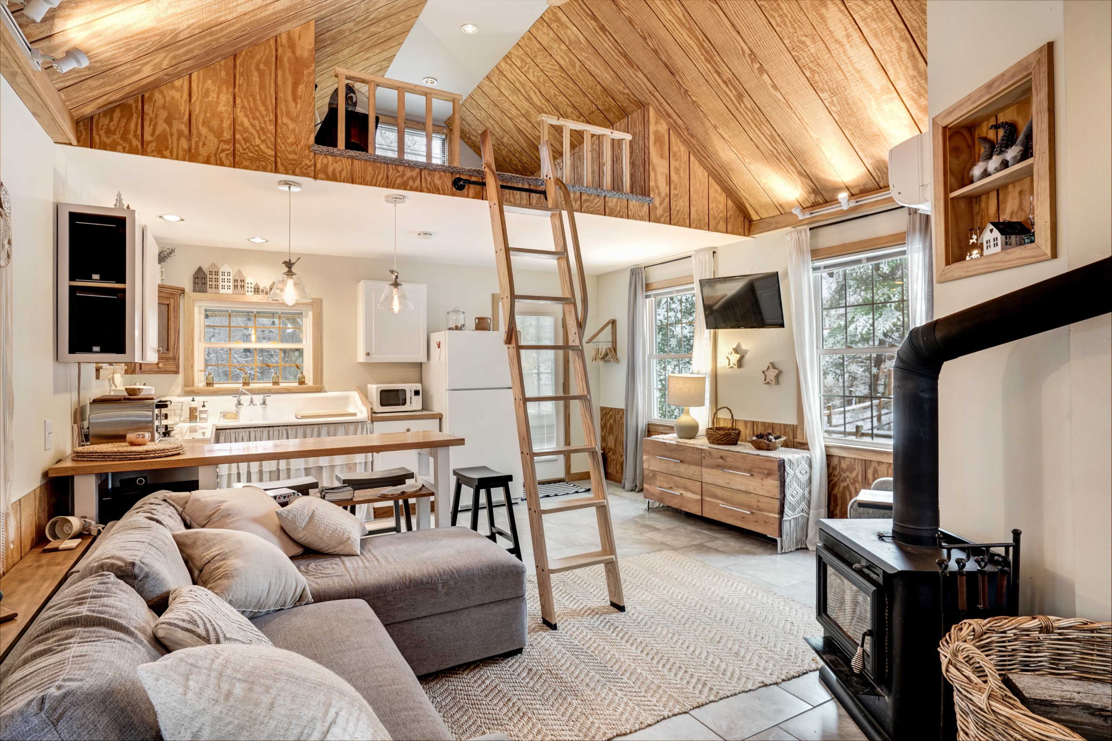 A modern, open-concept living space with a high wooden ceiling, a lofted area, and a cozy seating arrangement near a wood-burning stove.