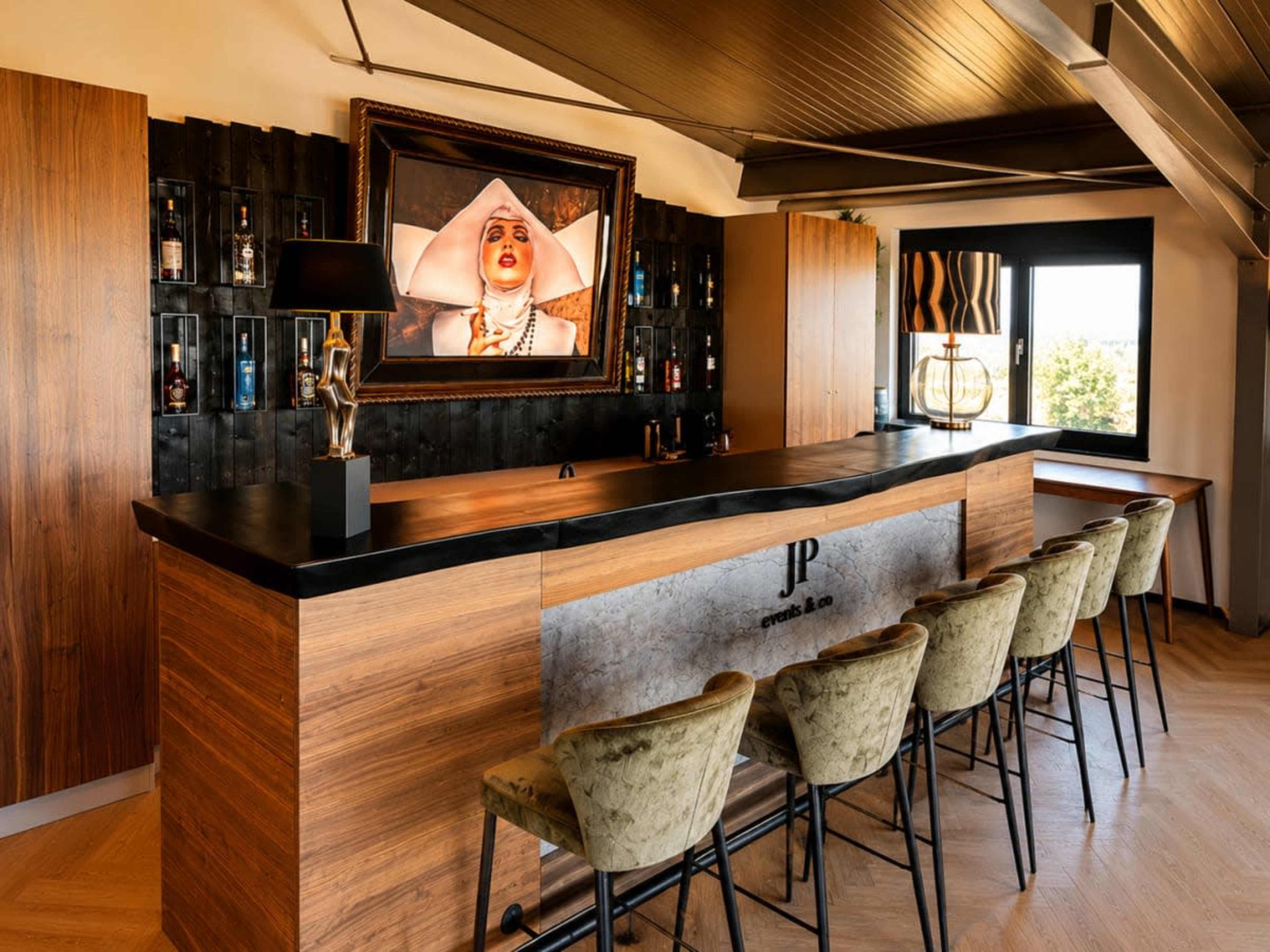 The image shows a modern bar area featuring a dark wood counter, several high stools, and a large framed portrait on the wall above.