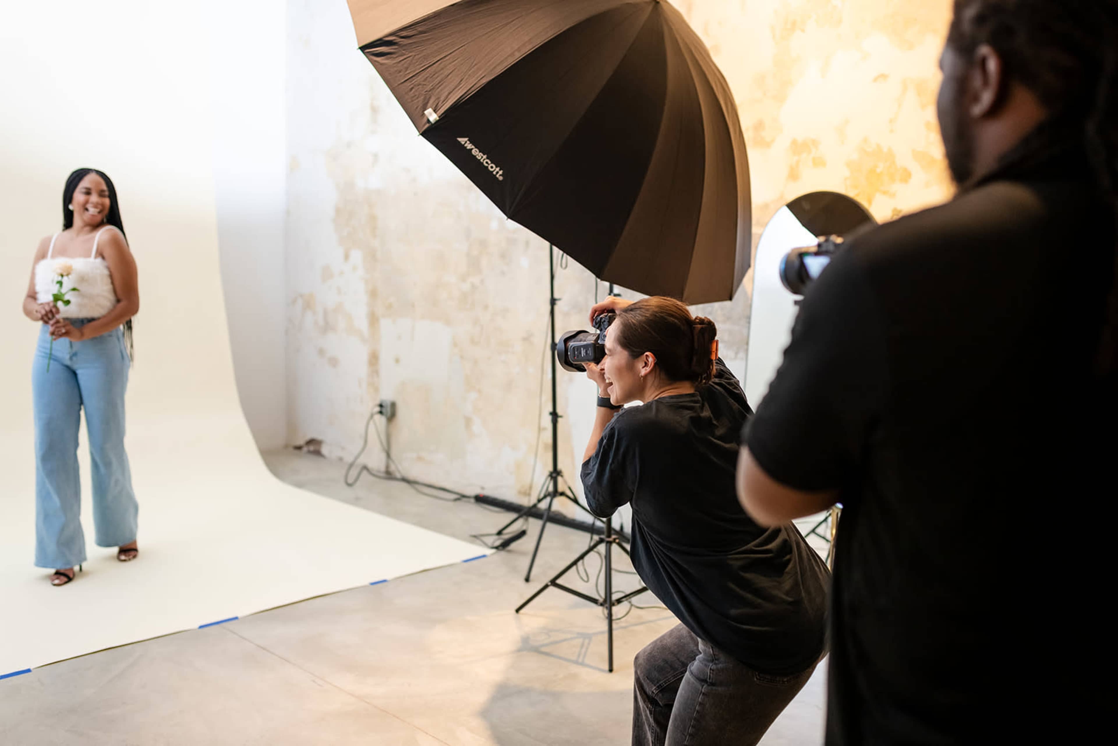 A photographer captures a model holding a flower in a studio setting with a large umbrella light.