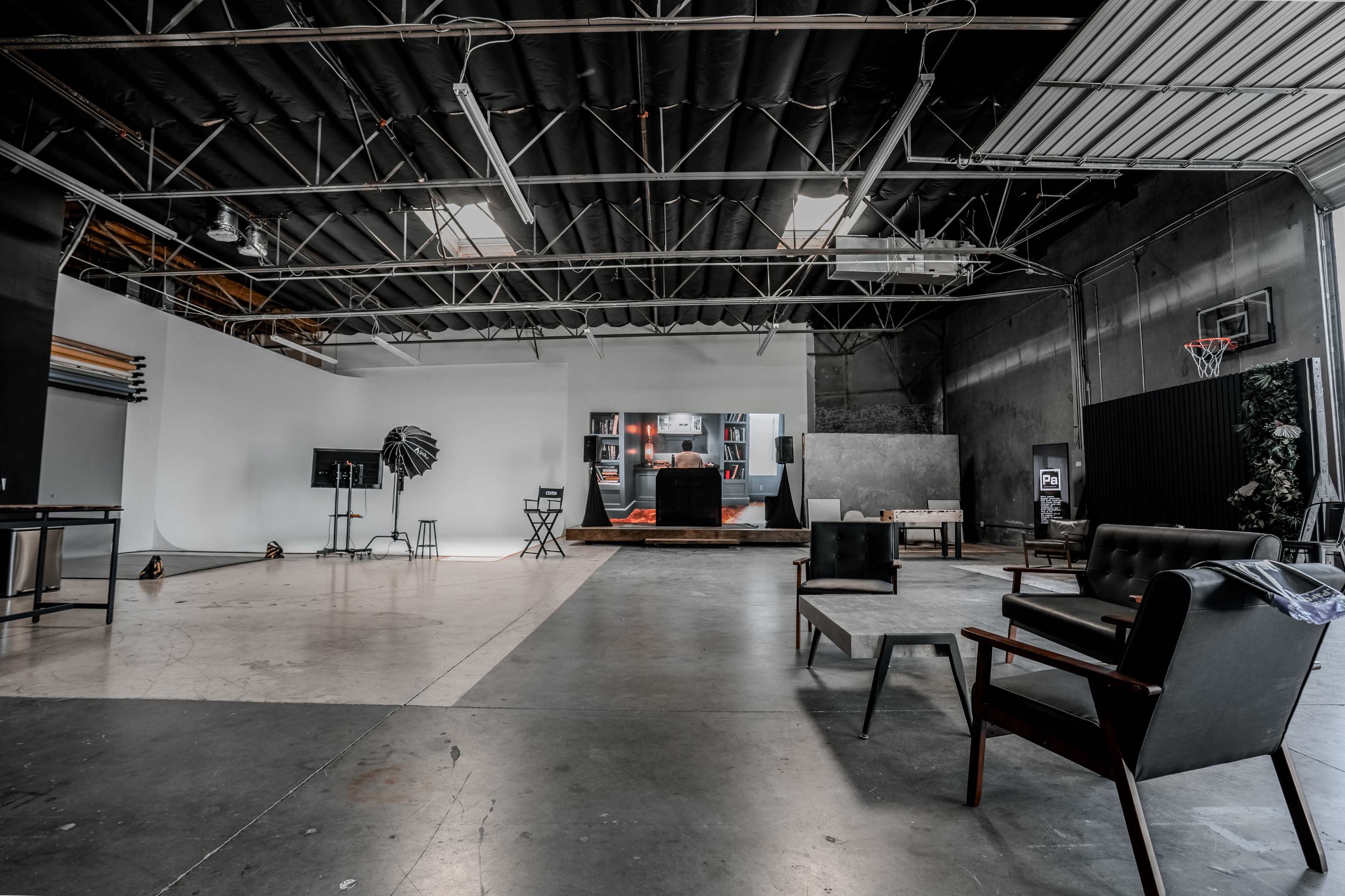 The image shows a spacious studio with a polished concrete floor, various seating options, and a distinct lighting setup in a minimalist environment.