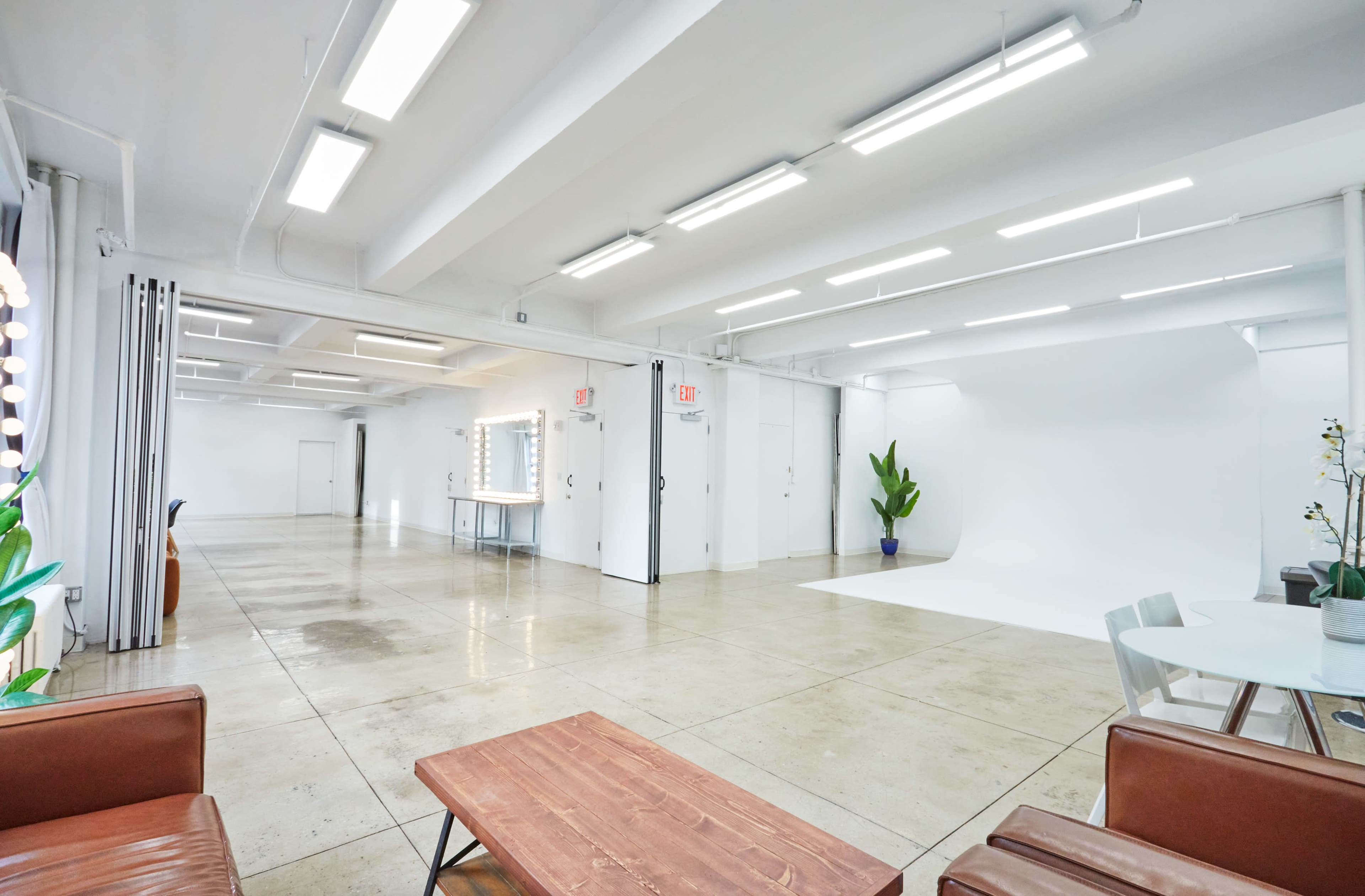 The image shows a spacious, well-lit studio with polished concrete floors and minimalistic white walls, featuring a seating area and a backdrop for photography.