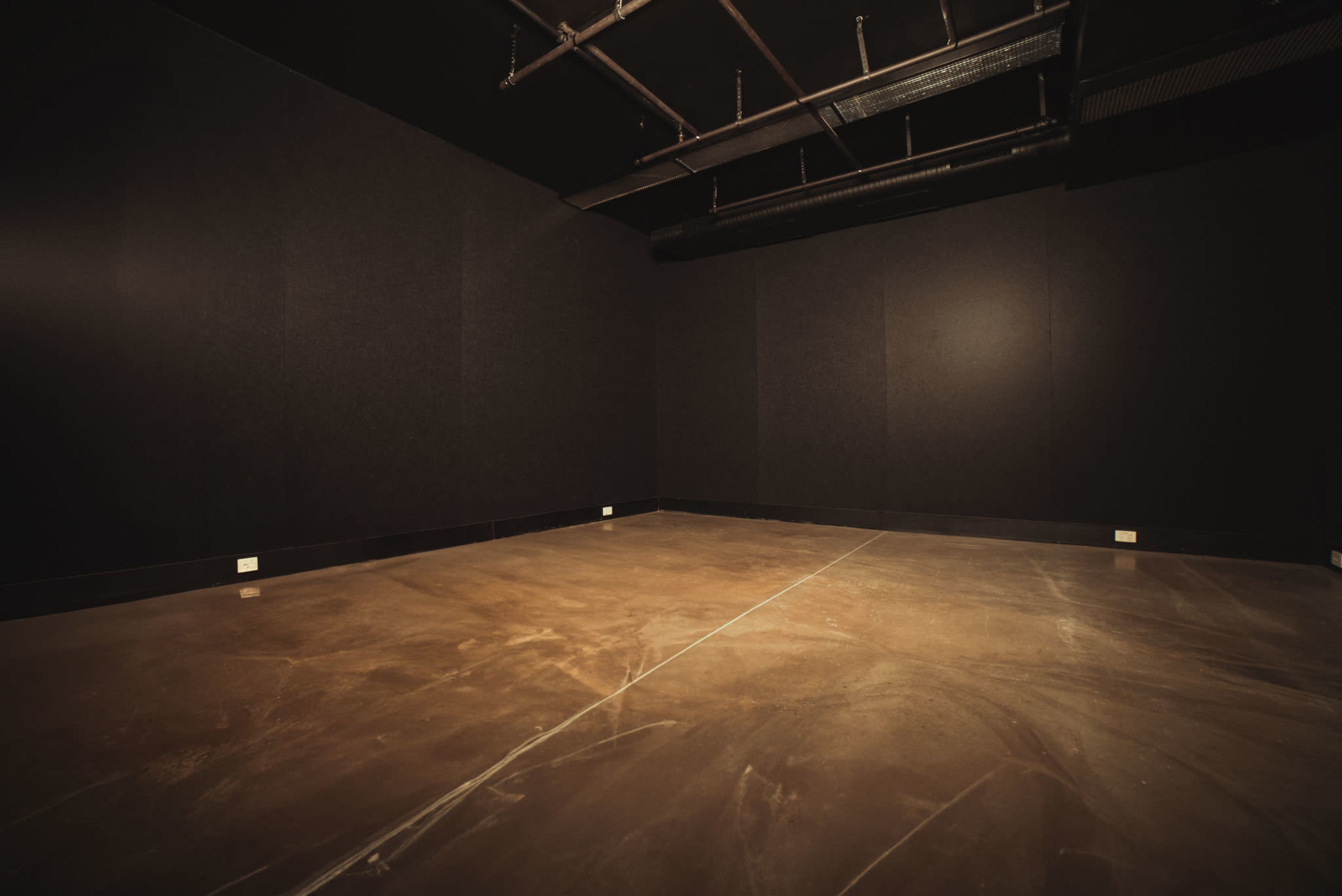 A dimly lit, empty room with black walls and a concrete floor.