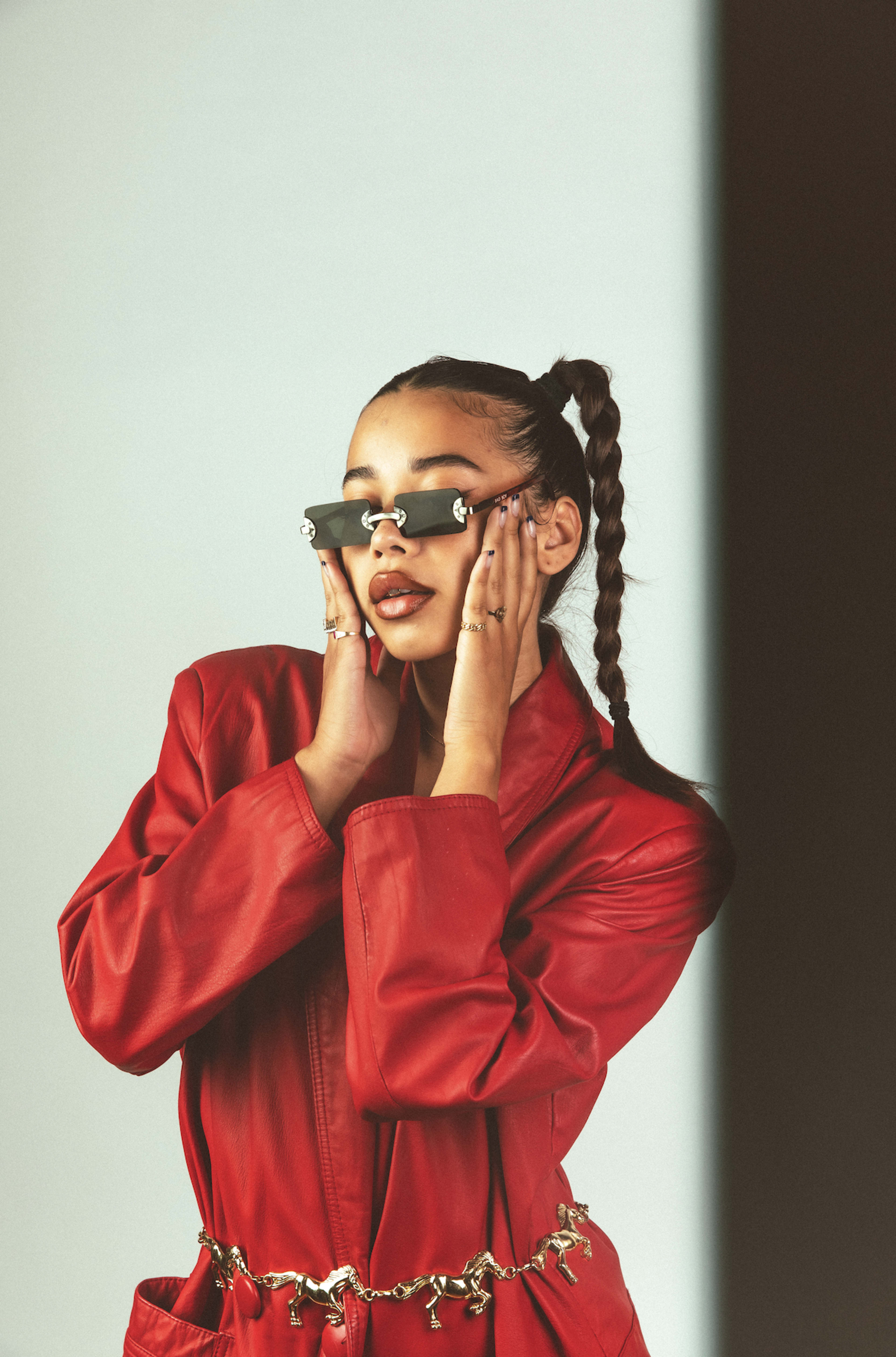 A fashion photoshoot featuring a woman in a red jacket holding a pair of sunglasses.