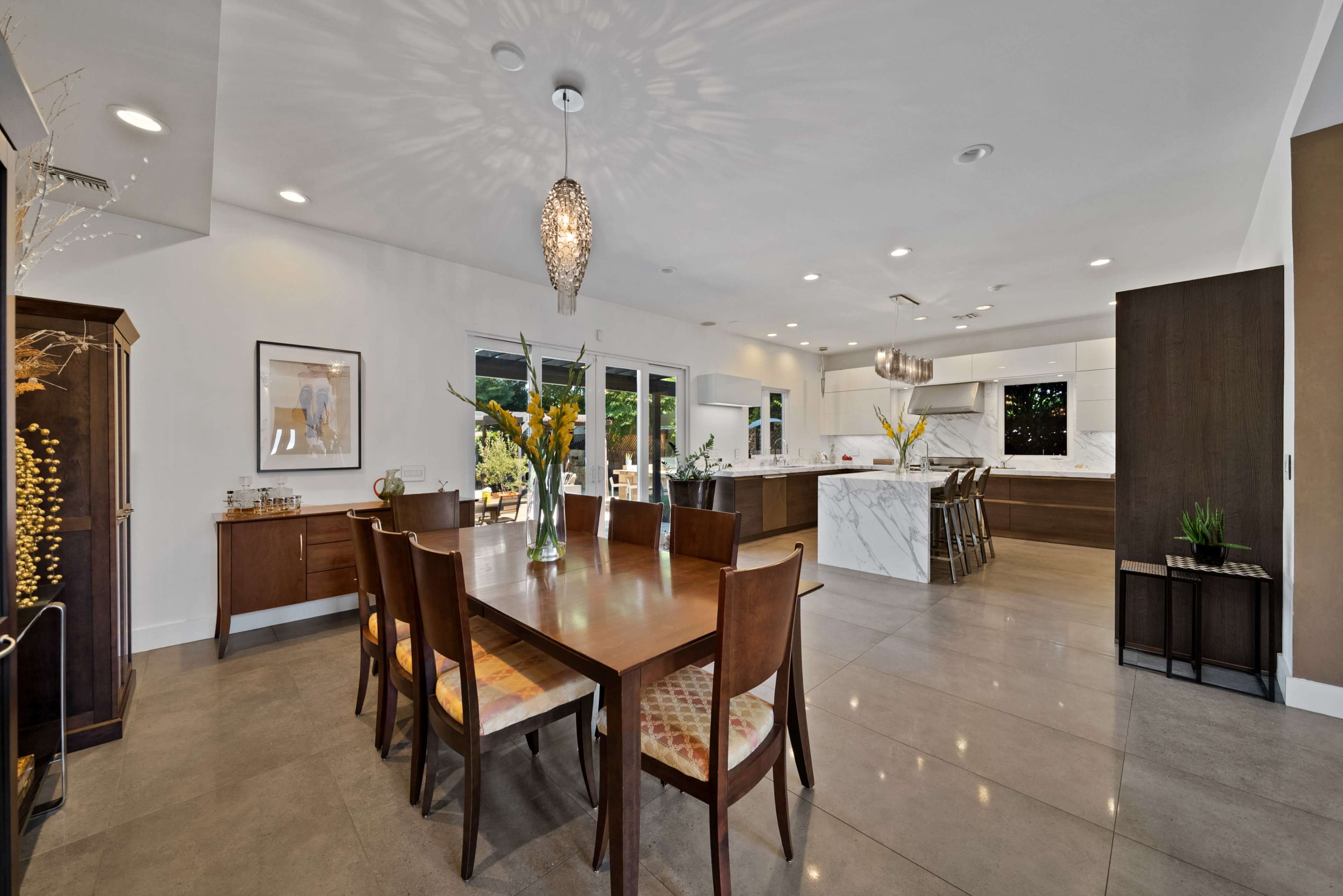 A modern dining area features a large wooden table surrounded by brown chairs, with a spacious kitchen visible in the background.