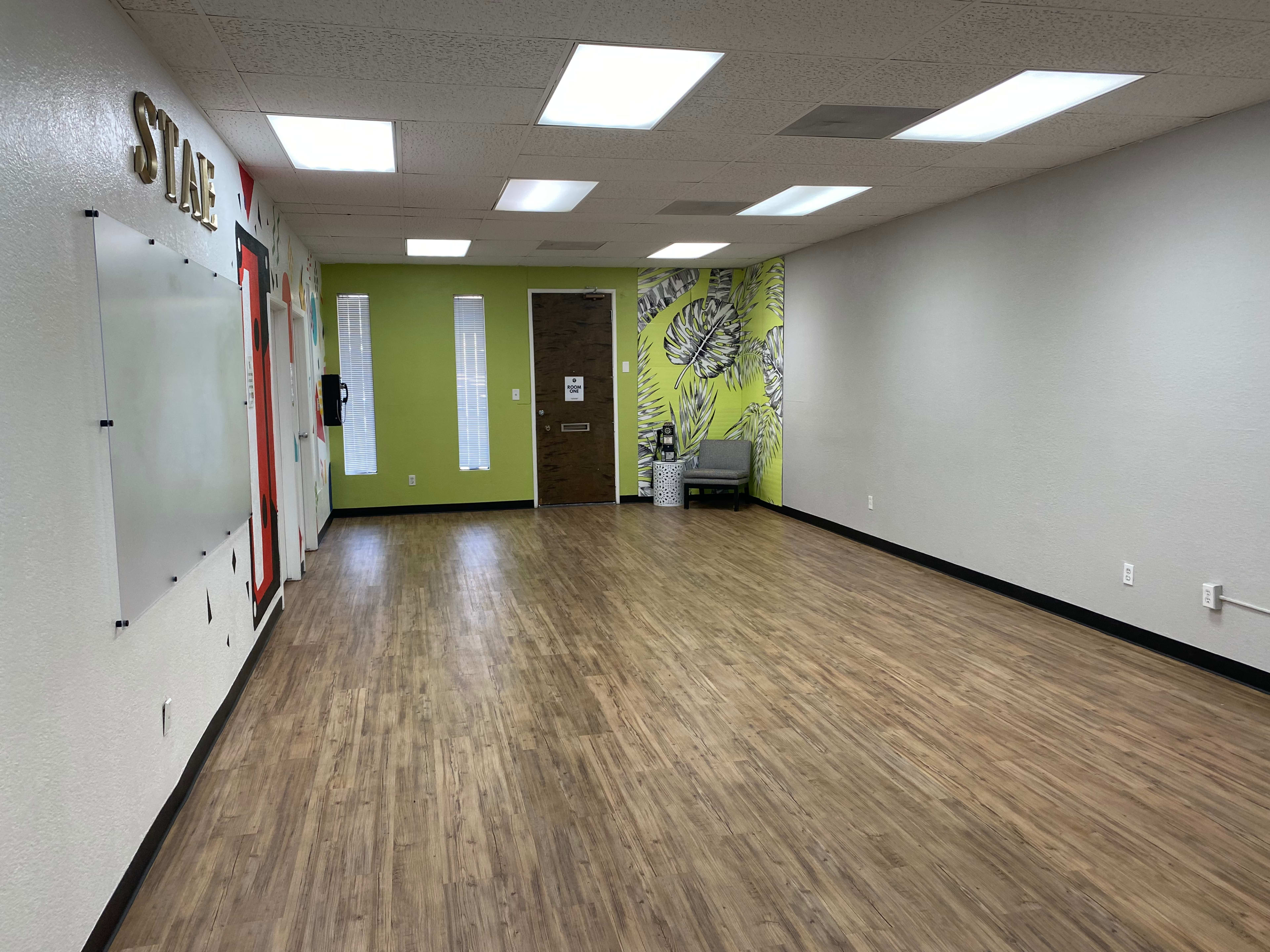 The image shows an empty room with wooden flooring, light gray walls, a green accent wall, and a door with windows at one end.