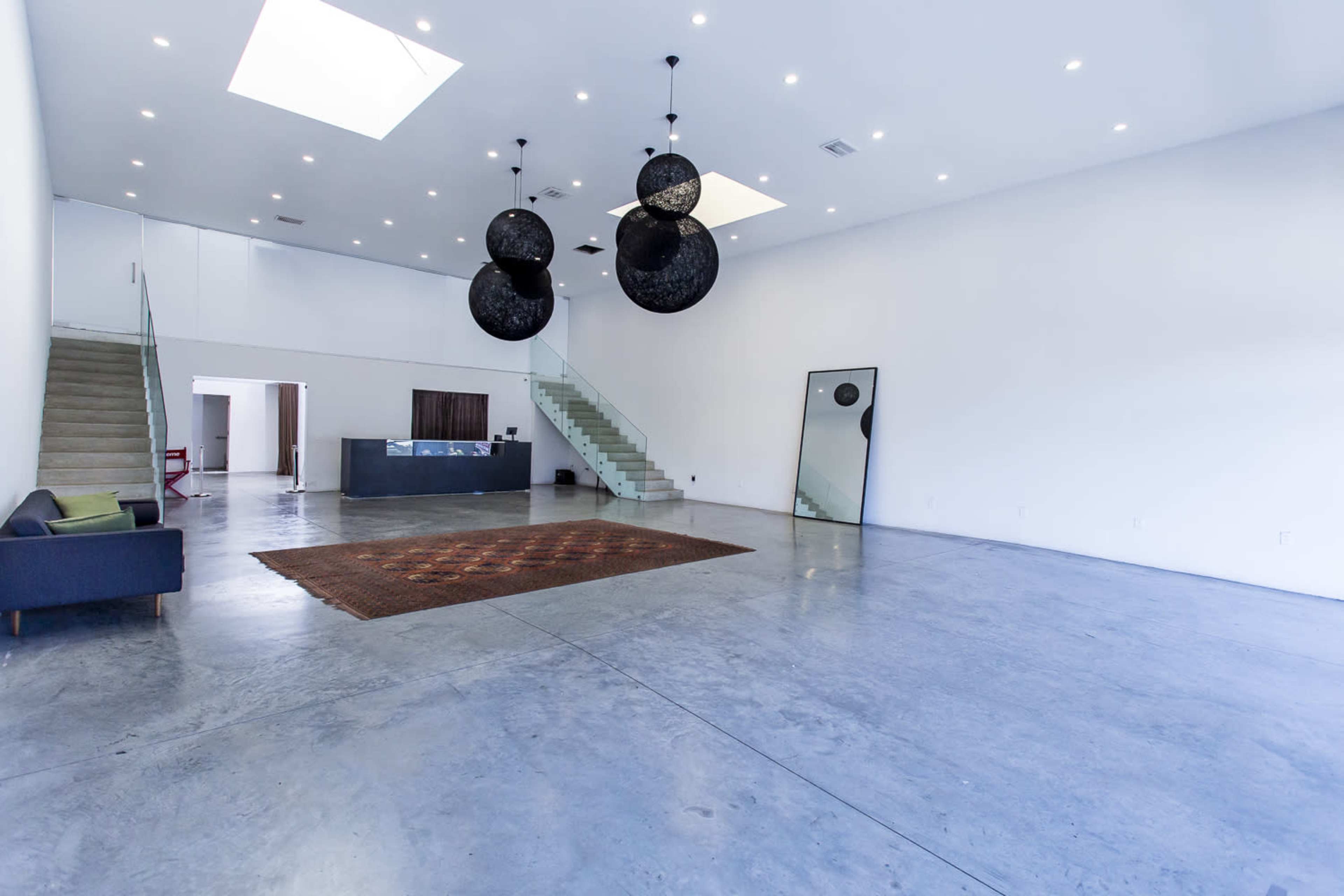 The image shows a spacious, modern interior with a polished concrete floor, large windows, a staircase, and three round pendant lights hanging from the ceiling.