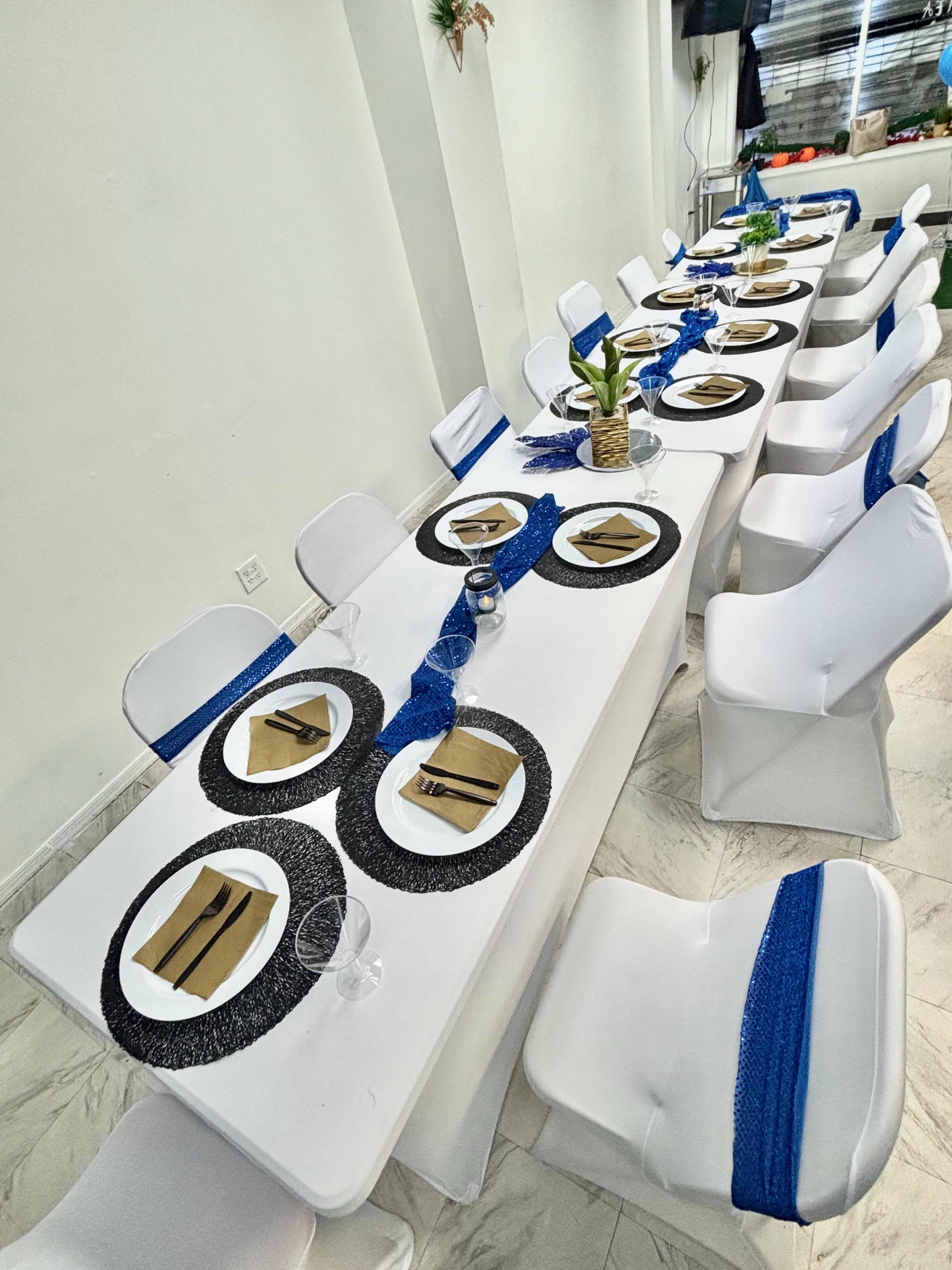 A long dining table is set with white tablecloths, black and blue decorations, and neatly arranged tableware.