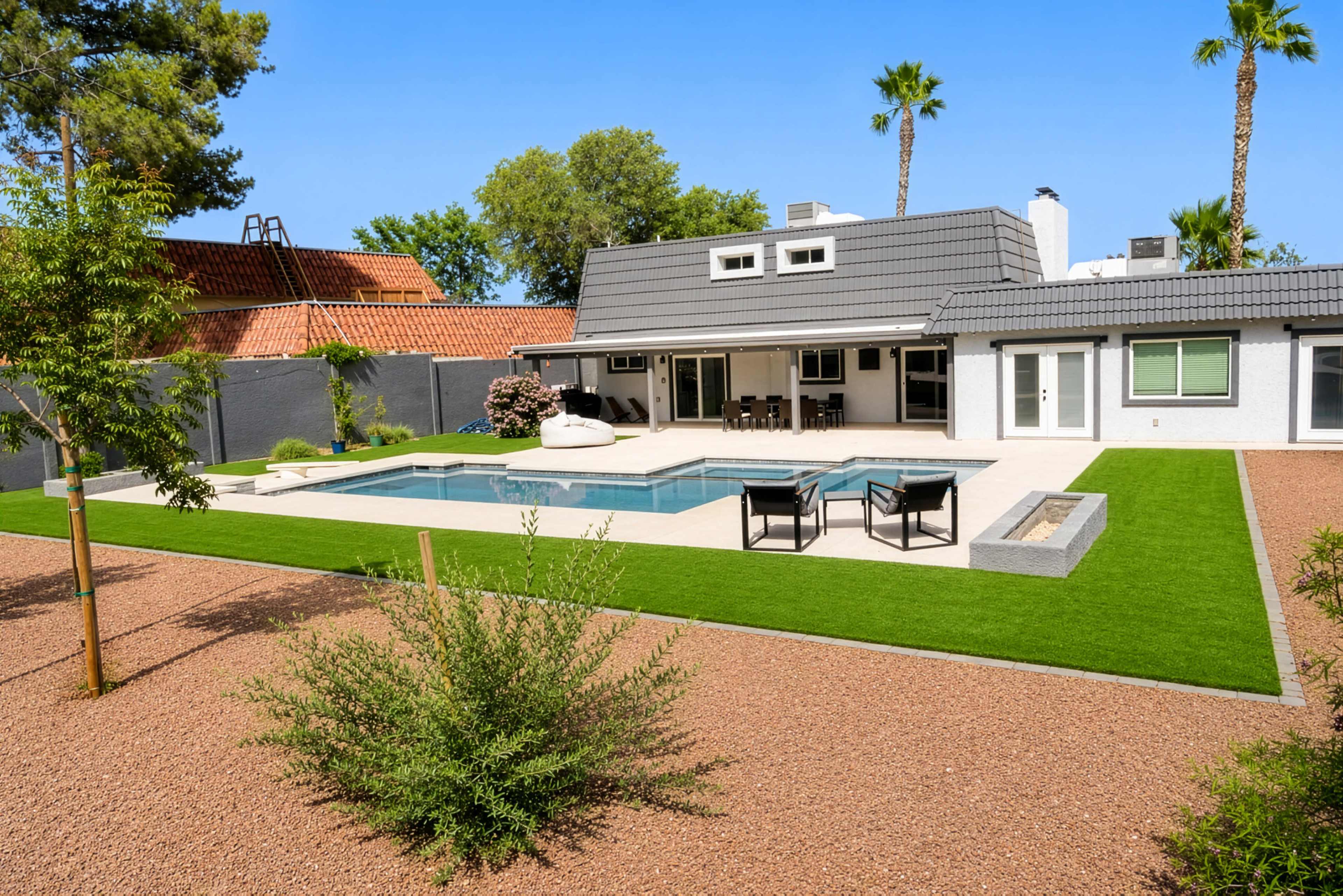 A modern house with a swimming pool is surrounded by landscaped gravel and greenery.