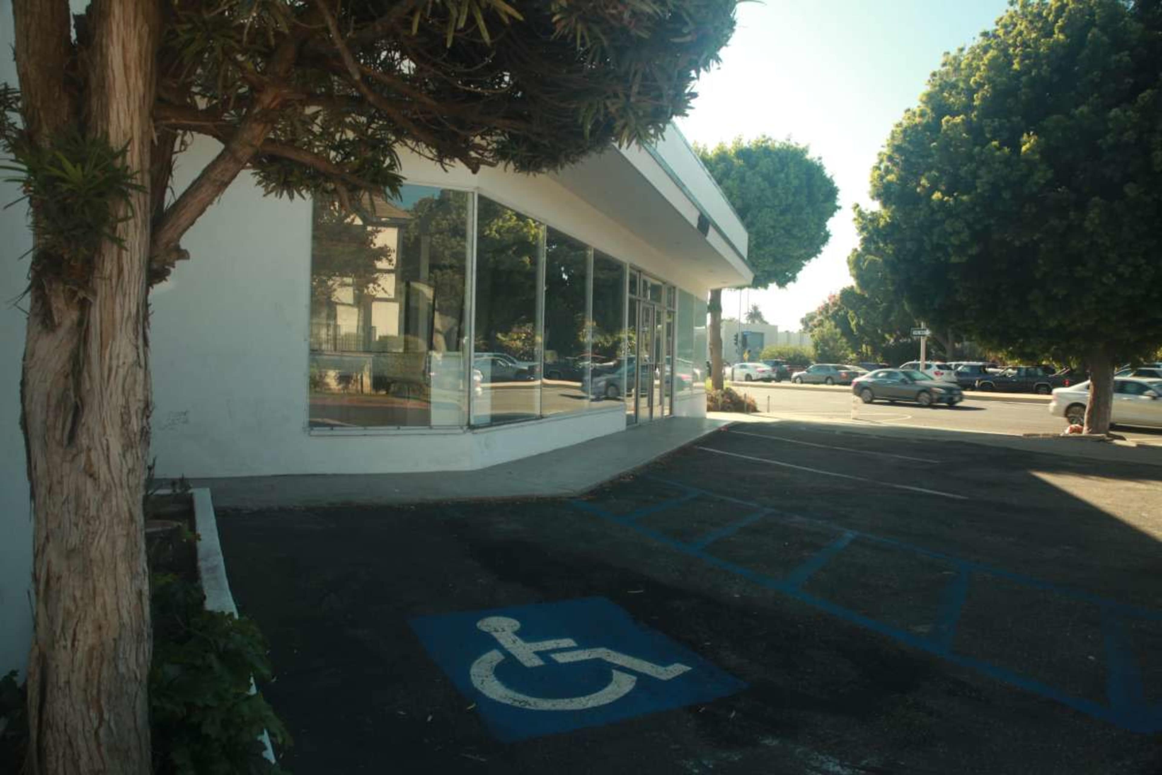 The image shows a parking lot with a designated disabled parking space and a view of a building with large windows.