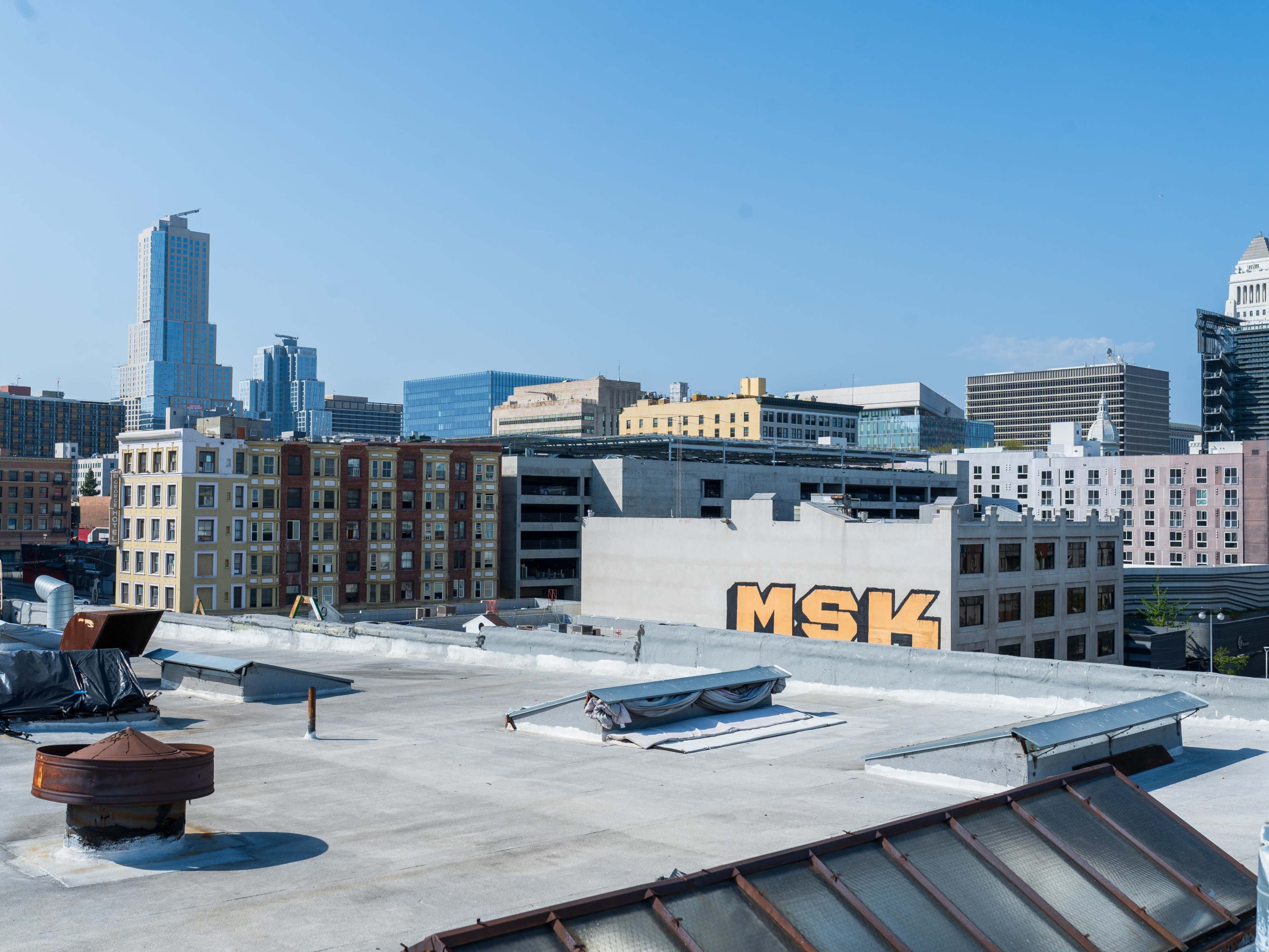 The image shows a view of urban rooftops with a prominent building displaying the letters "MSK" against a clear blue sky.