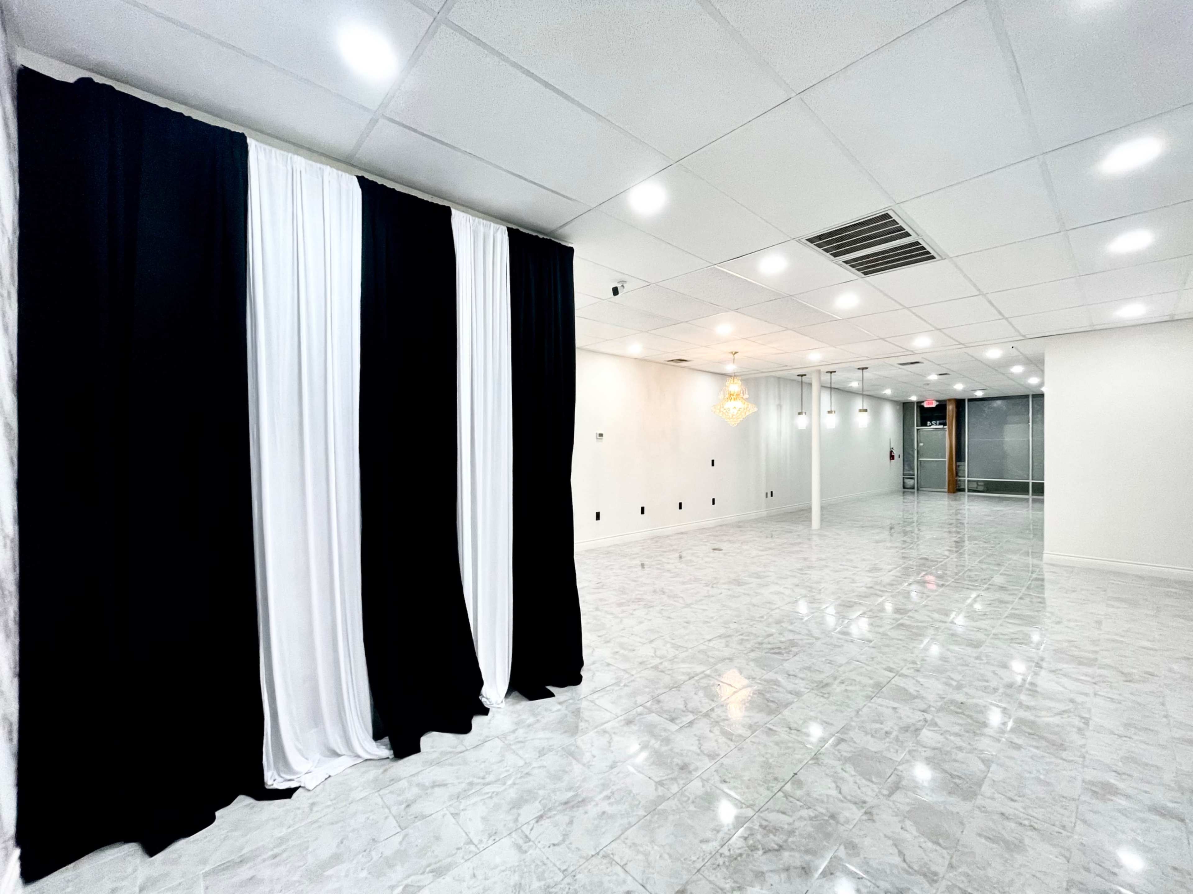 A spacious room with a glossy tiled floor, featuring a backdrop of black and white curtains on one side and a chandelier hanging from the ceiling.
