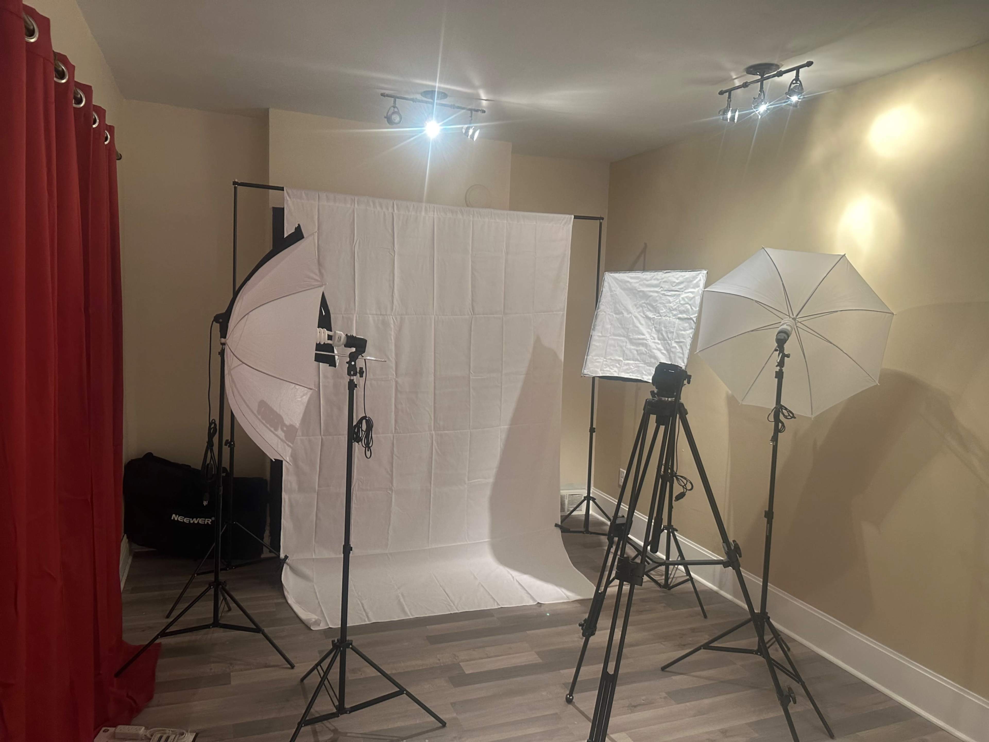 The image shows a photo studio setup with multiple light sources, a white backdrop, and tripods arranged in a room.